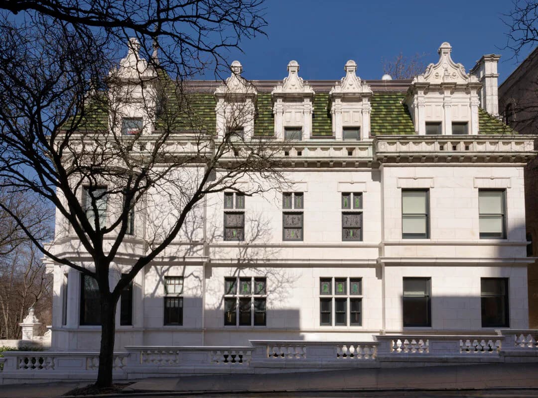Elegant neoclassical facade with cream-colored stone, ornamental roofline, and manicured landscaping by Charlotte Worthy Architects.