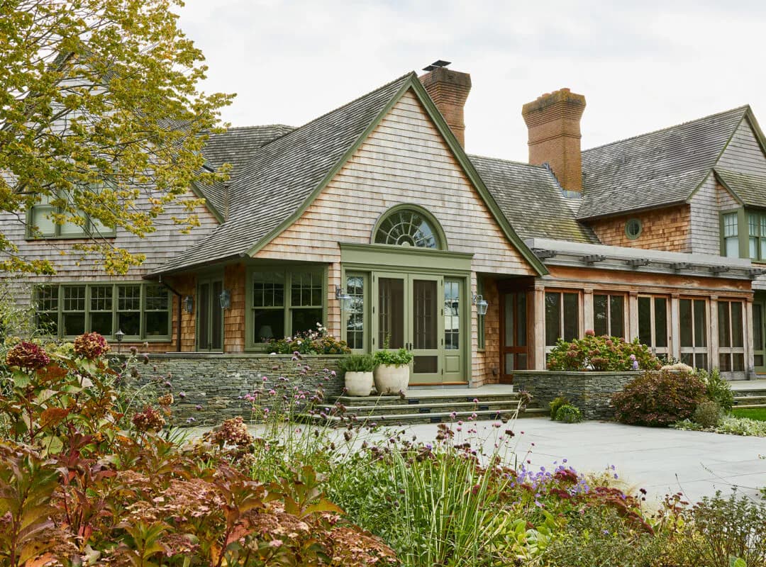 Contemporary residential exterior with mixed stone and siding, gabled rooflines, and manicured landscaping by Charlotte Worthy Architects.
