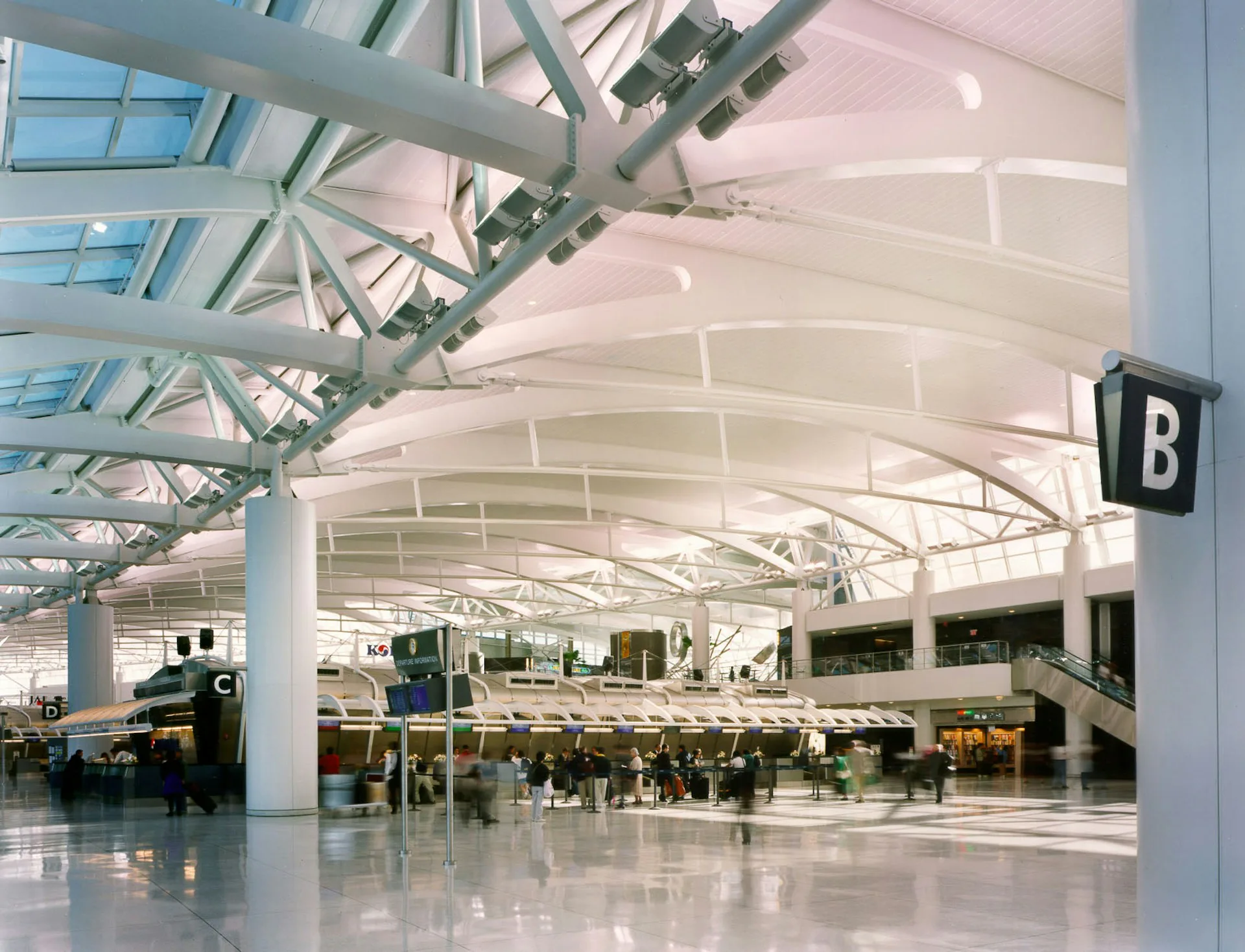 Expansive airport terminal with soaring white barrel-vault ceiling, steel trusses, skylights, polished floors, and minimal columns by Chelsea Atelier Architect, PC.