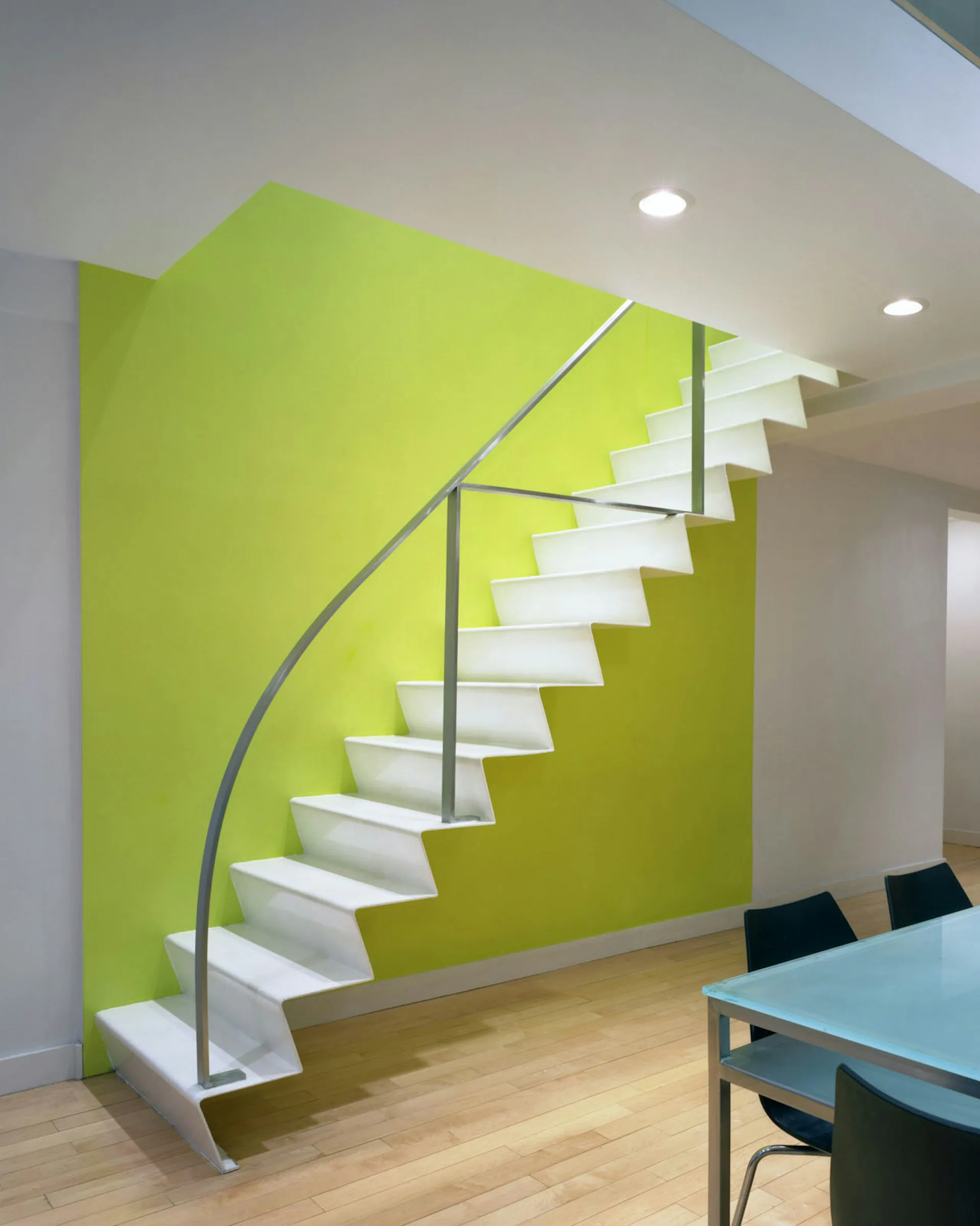 Modern staircase with white steps and metal railings against a vibrant lime-green wall, featuring crisp synthetic lighting and idealized material finishes by Chelsea Atelier Architect, PC.