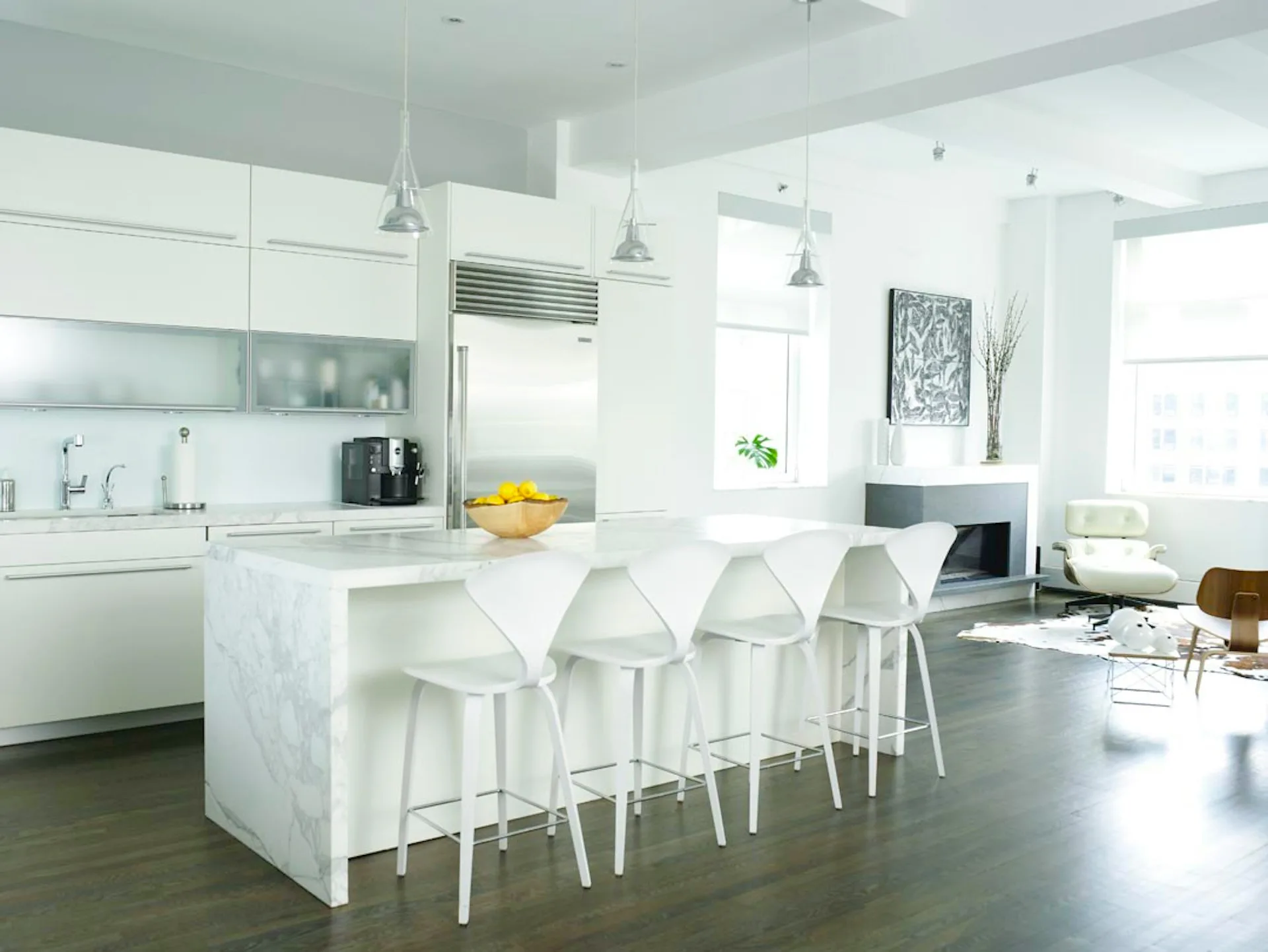 Bright modern kitchen with white cabinetry, marble waterfall island, pendant lighting, and open living area with gray flooring by Chelsea Atelier Architect, PC.