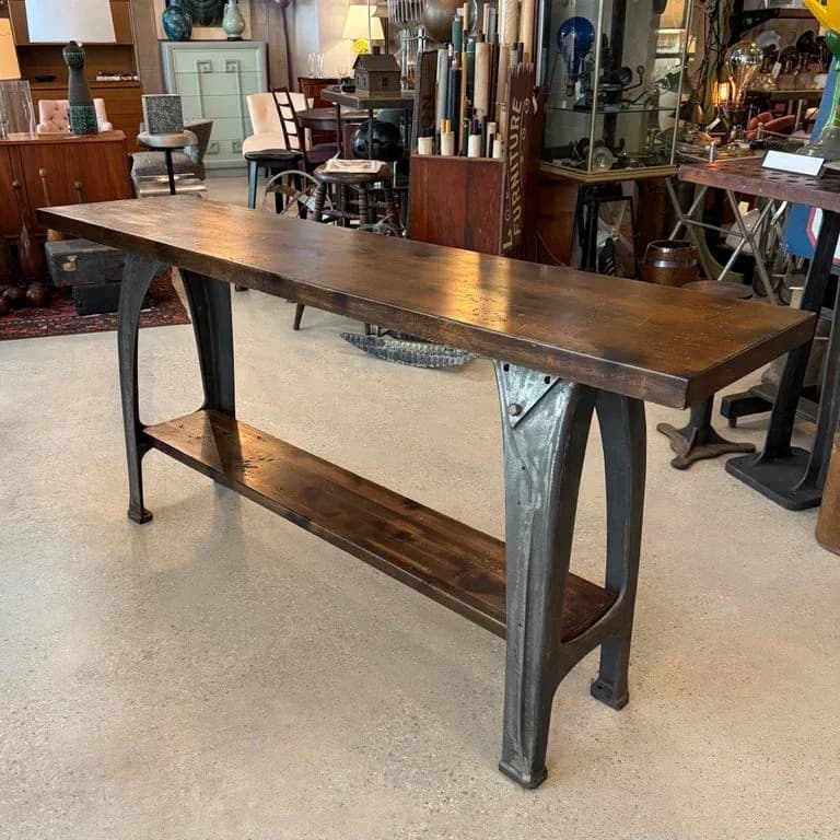 Industrial-style console table with dark metal base and warm wood top displayed in a showroom setting by cityFoundry.