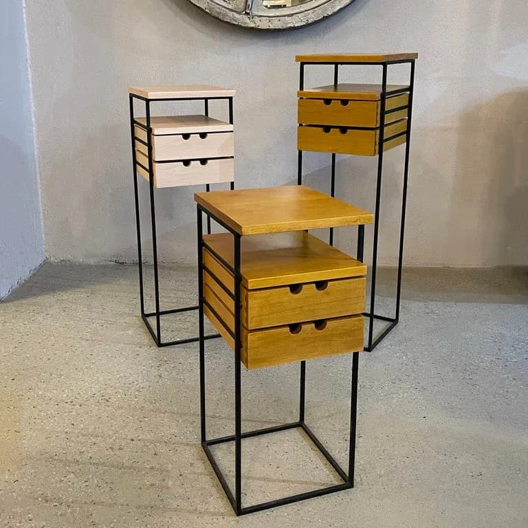Three modular storage units with black metal frames and wooden drawers in natural and yellow finishes, displayed in a minimalist gallery setting by cityFoundry.