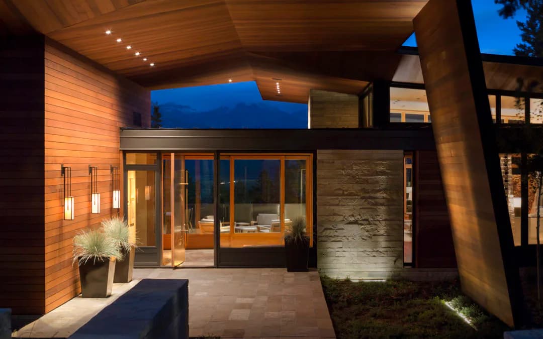 Modern residential entry featuring warm wood cladding, concrete cylindrical column, and glazed doors illuminated by architectural lighting design by Cline Bettridge Bernstein Lighting Design (CBB).