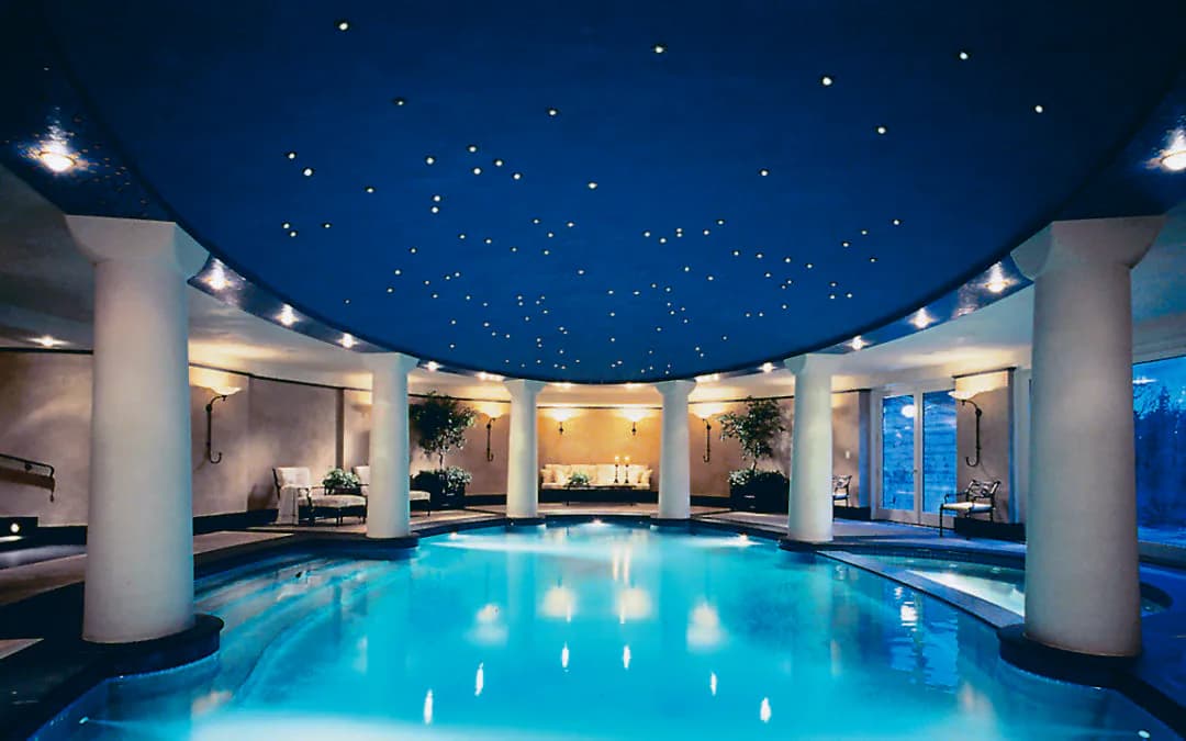 Luxurious indoor swimming pool with illuminated ceiling stars, columns, and ambient blue lighting designed by Cline Bettridge Bernstein Lighting Design (CBB).