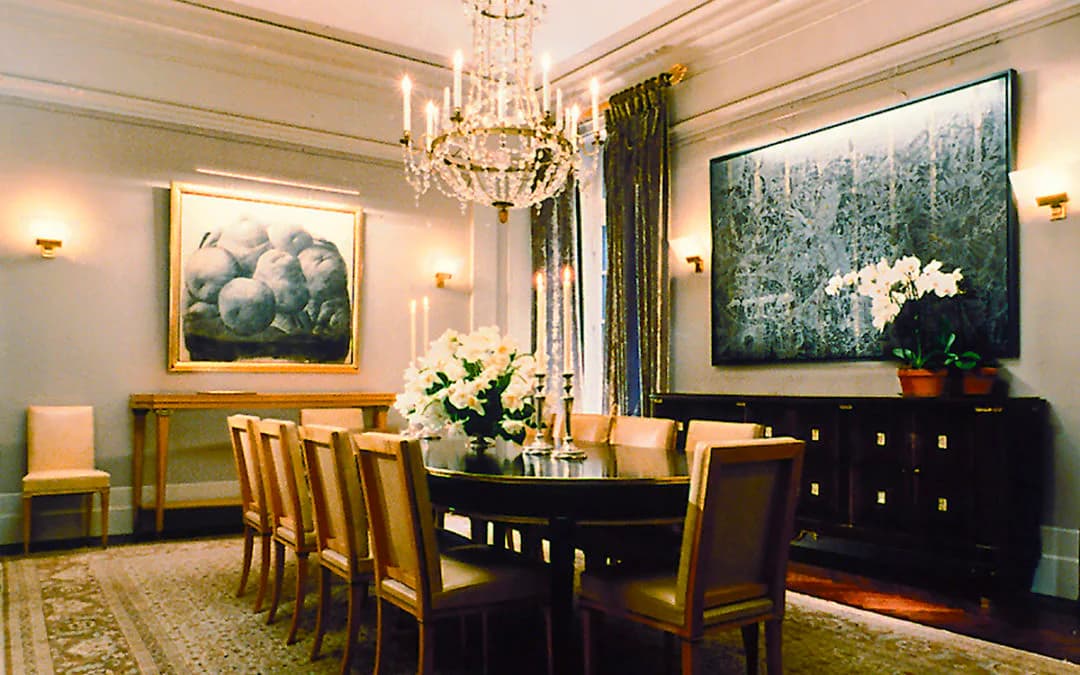 Elegant formal dining room with black table, gold-accented chairs, crystal chandelier, and gallery-style artwork lighting by Cline Bettridge Bernstein Lighting Design (CBB).