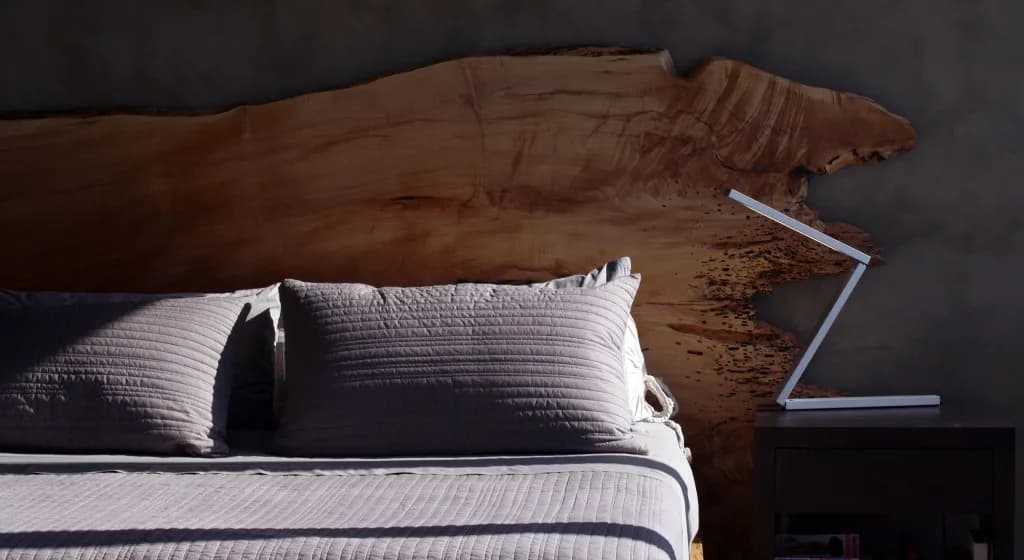 Modern bedroom interior featuring a wooden headboard, white striped bedding with pillows, and minimalist nightstand, designed by Clodagh Design.