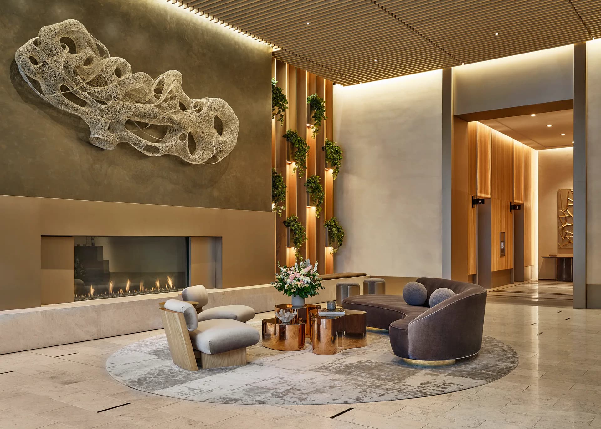 Luxury lobby interior with marble flooring, curved gray seating, vertical green wall installation, sculptural white ceiling art, and built-in fireplace by Clodagh Design.