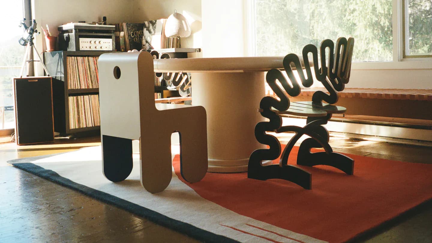 Warm wooden furniture and sculptural black pieces arranged on a rust-red rug in a bright studio space by Cold Picnic.