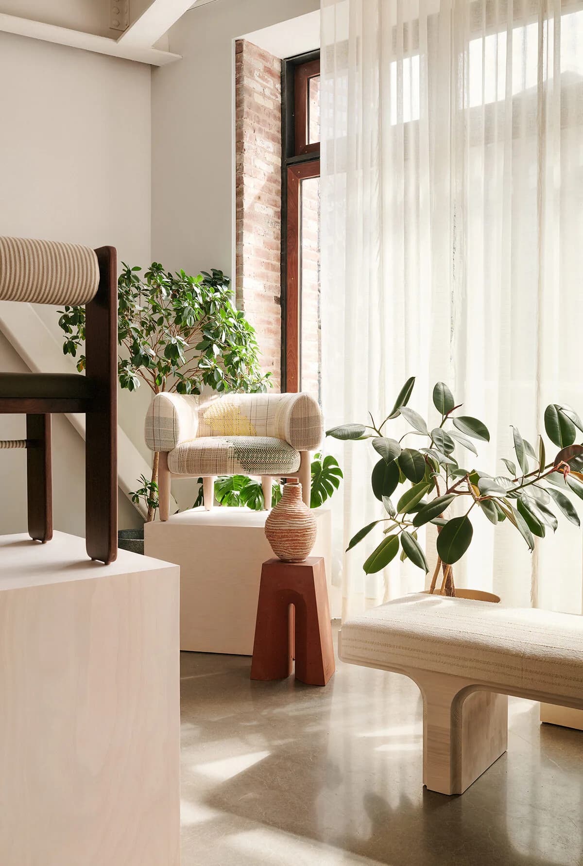 Bright, minimalist interior with cream upholstered chair, natural wood furniture, potted plants, and sheer white curtains flooding the space with sunlight by Colony.