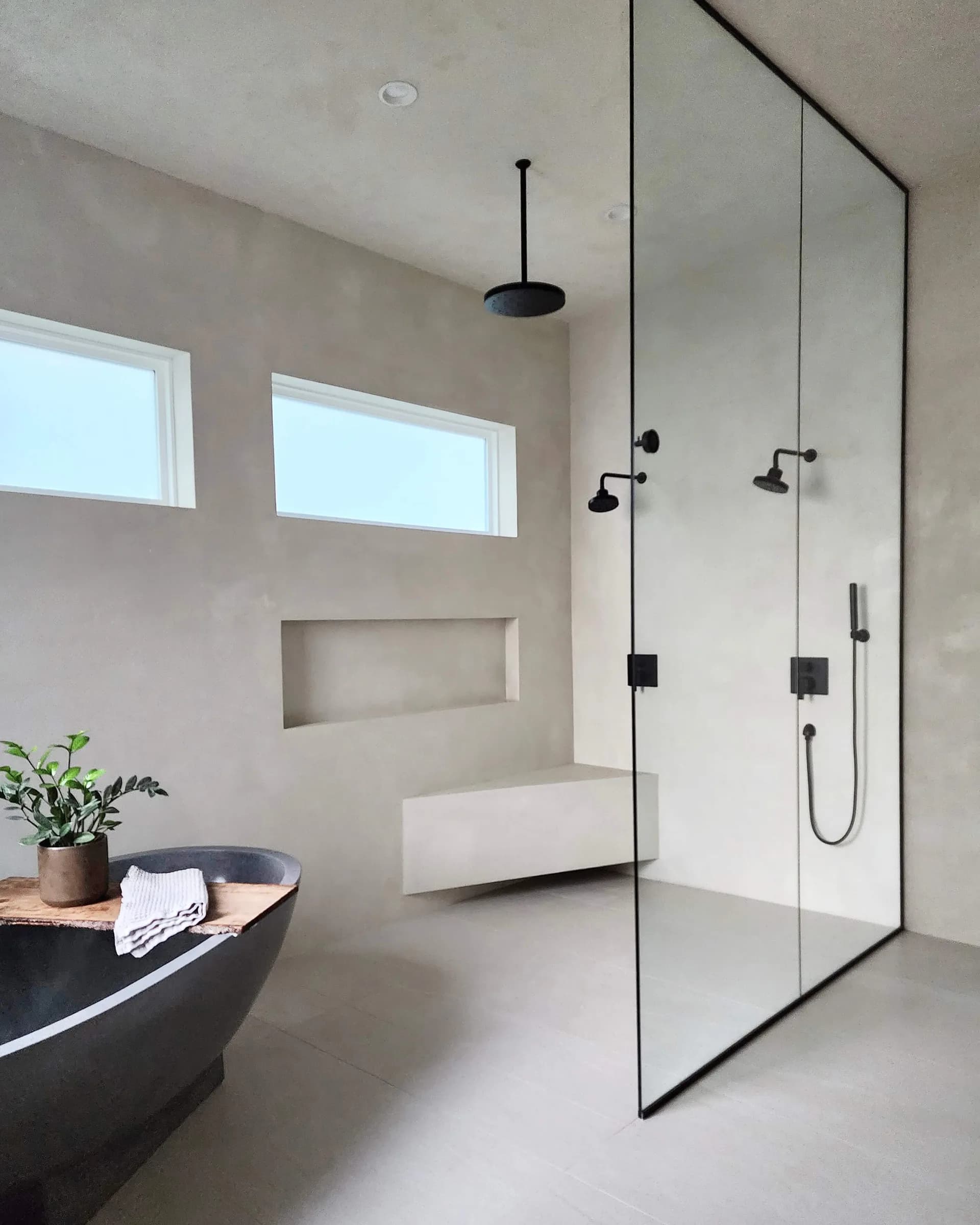 Modern minimalist bathroom with floating vanity, black soaking tub, and frameless glass shower enclosure with black fixtures by Color Atelier.