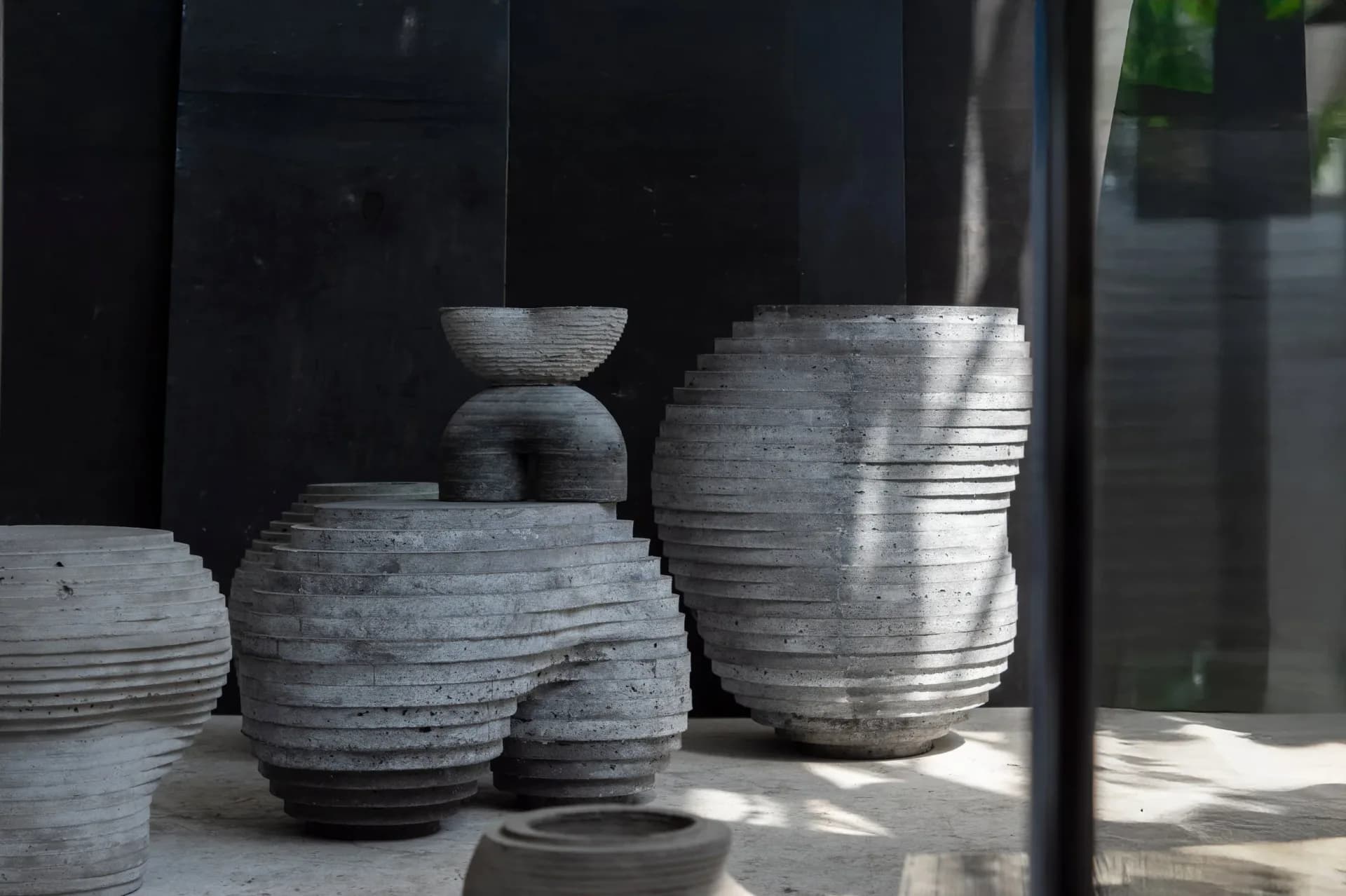 Sculptural ceramic vessels with textured ridged surfaces in grey and black tones, displayed in natural light by Concrete Poetics.