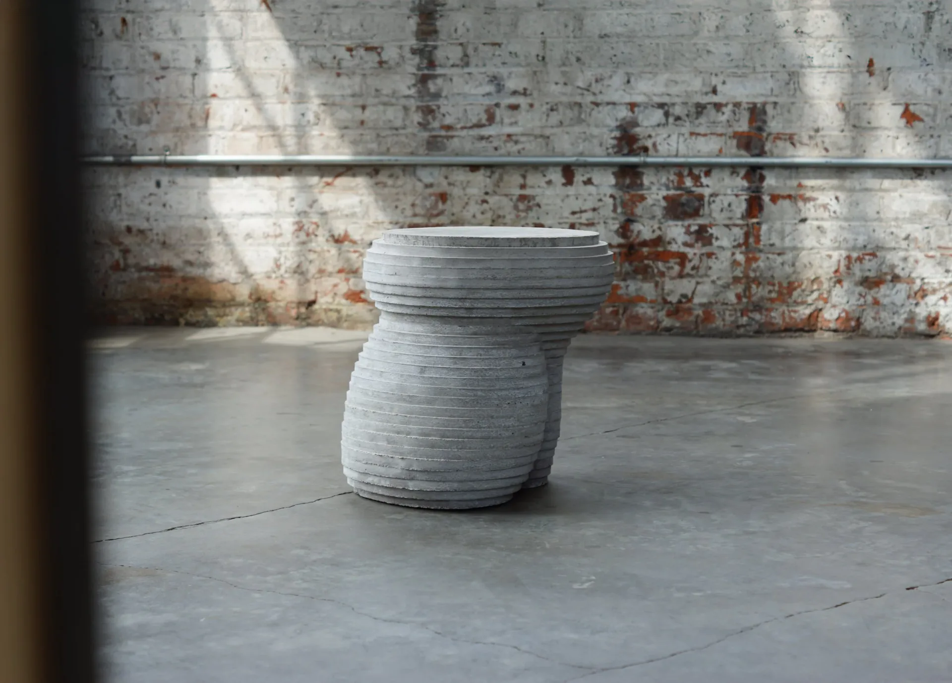 Sculptural concrete vessel with organic ribbed texture sits on polished concrete floor against weathered industrial backdrop by Concrete Poetics.