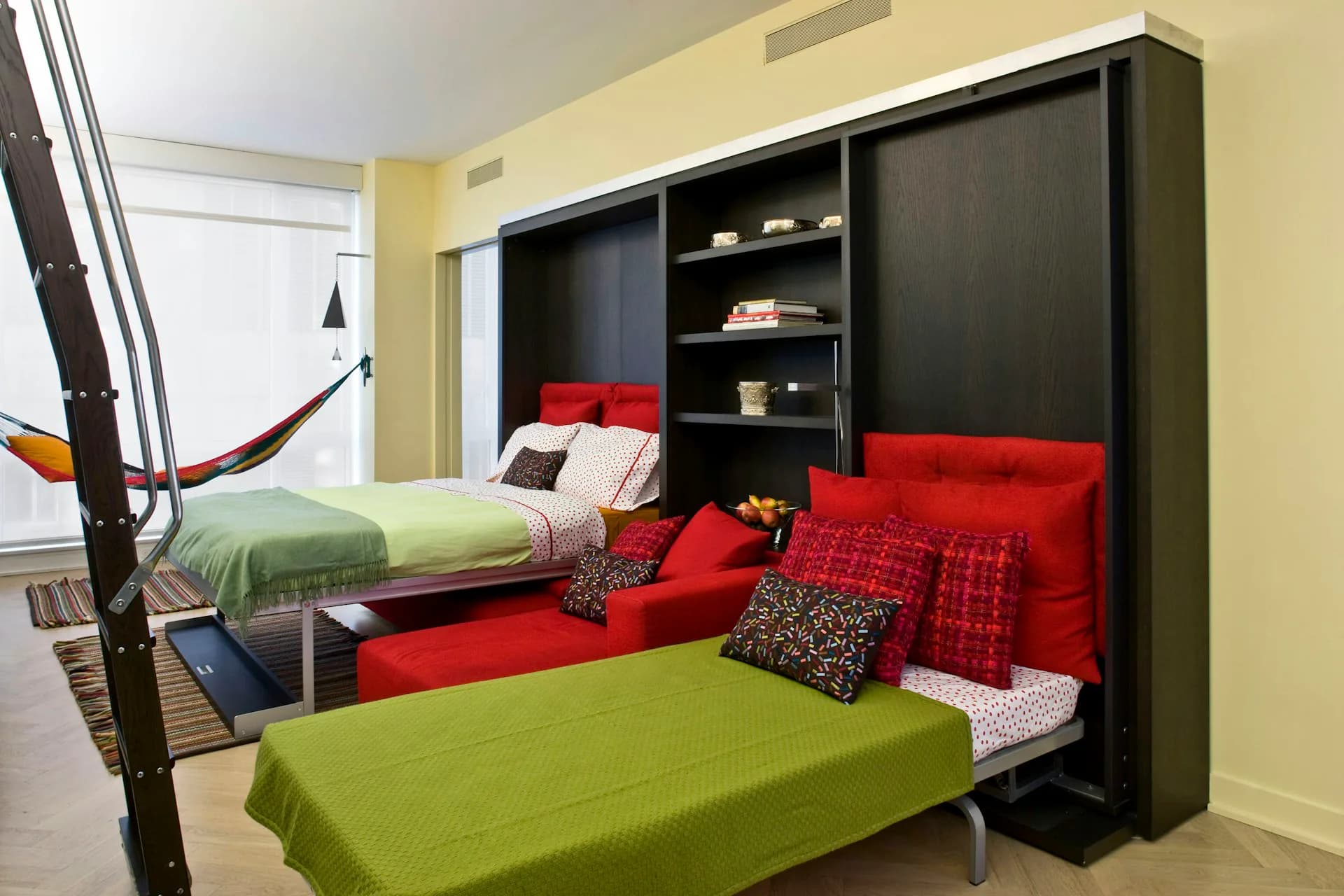 Multi-bed youth bedroom with black built-in cabinetry, green and red upholstered beds, yellow walls, and integrated storage by Construct Architecture Studio, PC.