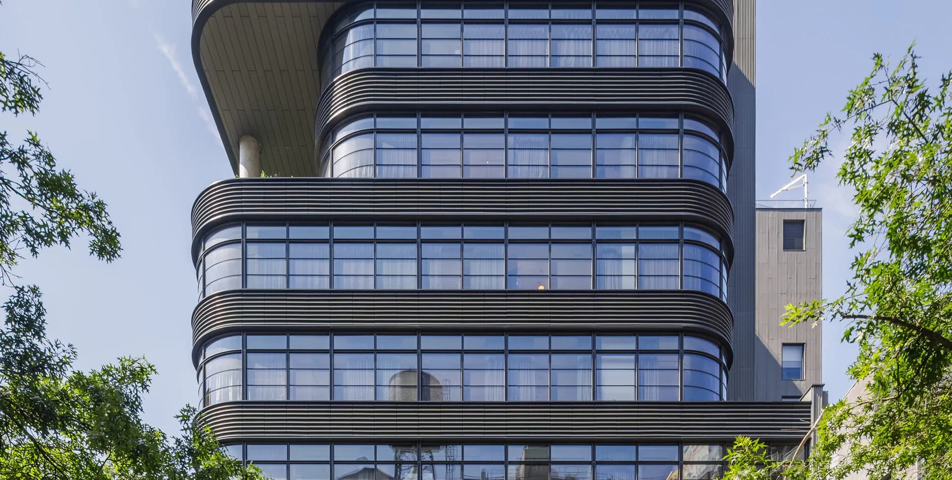 Curved glass and metal facade of a modern residential tower with stacked horizontal balconies and ribbon windows by COOKFOX Architects.