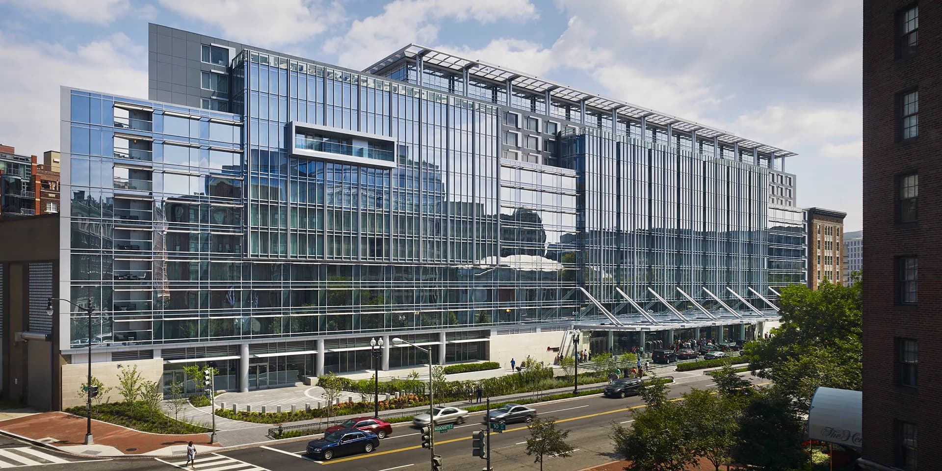 Modern multi-story glass and metal facade building with horizontal striping, ground-level plaza, and landscaping by Cooper Carry.