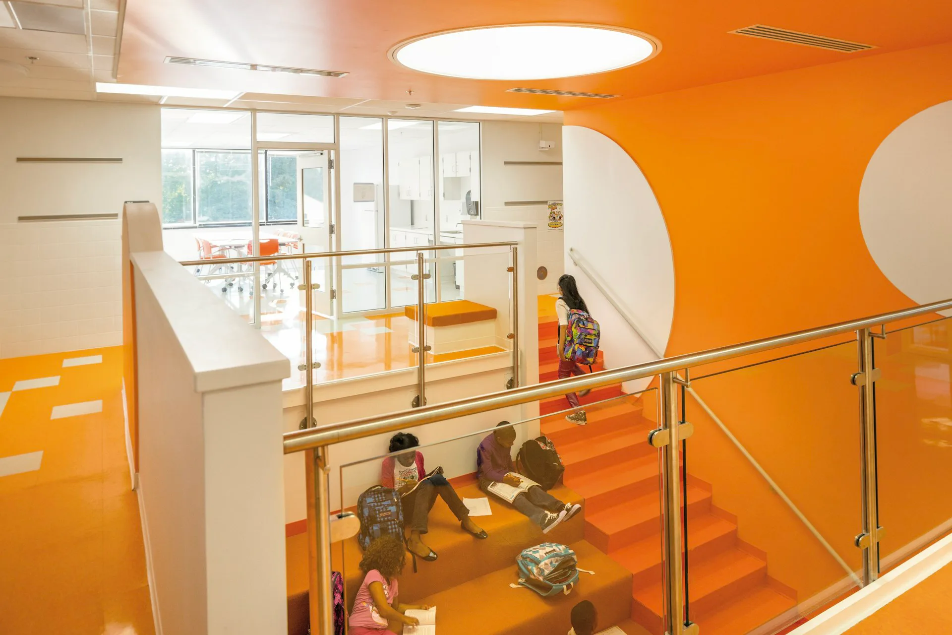 Bright orange and white multi-level interior with modern staircase, glass railings, and contemporary lighting design by Cooper Carry.