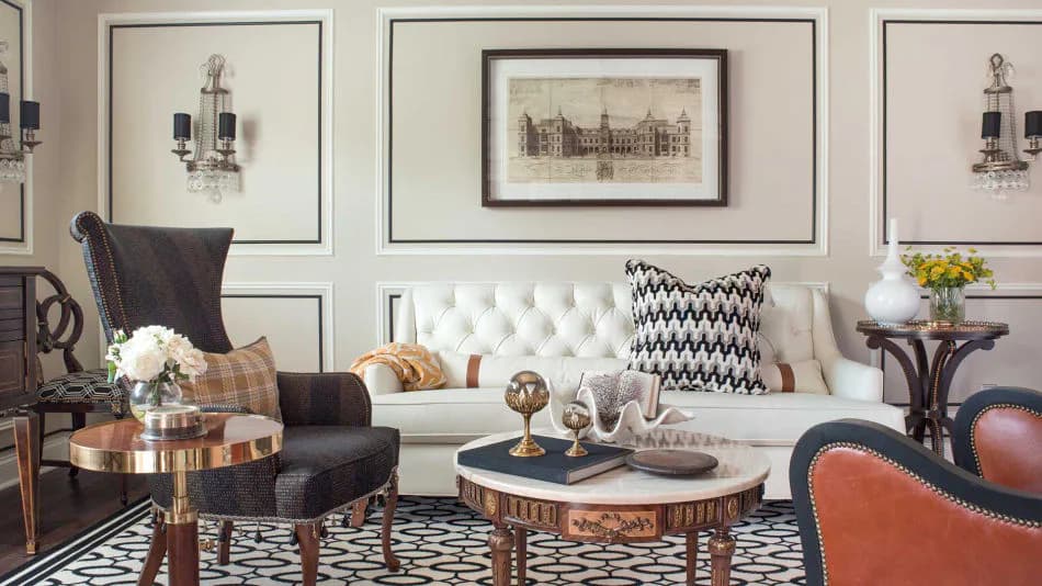 Elegant living room with white tufted sofa, black leather wingback chair, round wood-slice coffee table, geometric patterned rug, and framed architectural prints by Corey Damen Jenkins & Associates.