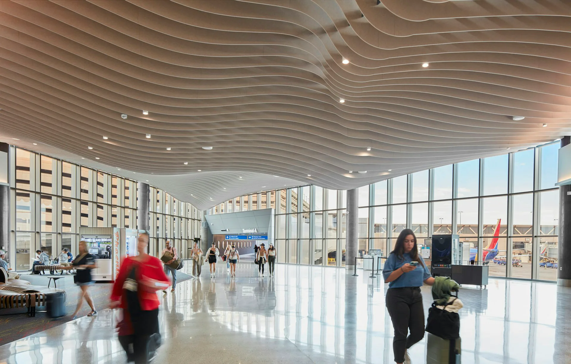 Bright, modern airport terminal with curved linear ceiling details, expansive glazing, polished floors, and minimal furnishings by Corgan.
