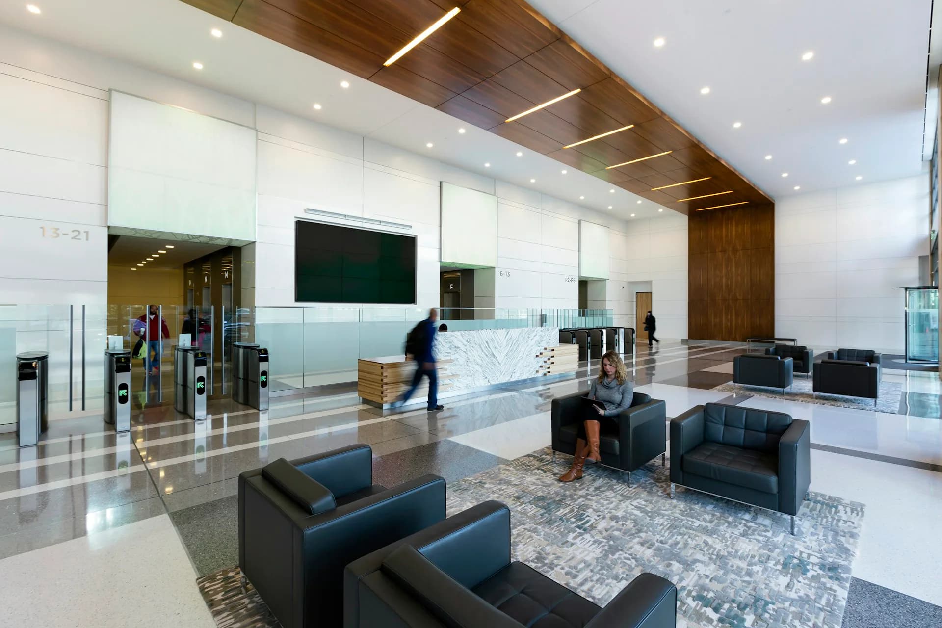 Modern corporate lobby featuring white walls, wood ceiling details, navy seating, and glass partitions with integrated lighting by Corgan.