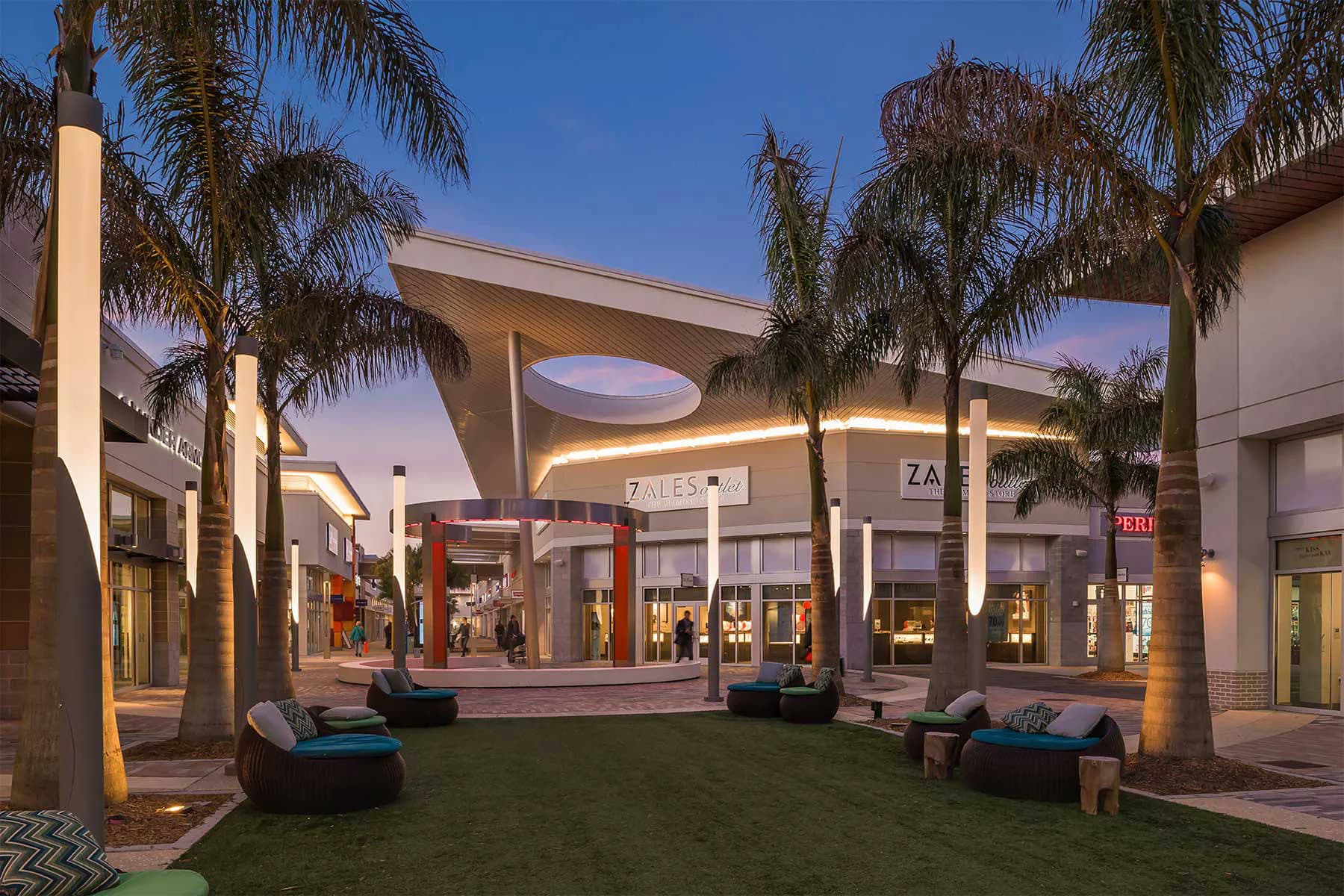Modern outdoor shopping pavilion with palm trees, illuminated curved ceiling, synthetic lighting, and polished surfaces designed by CREATE Architecture Planning & Design.