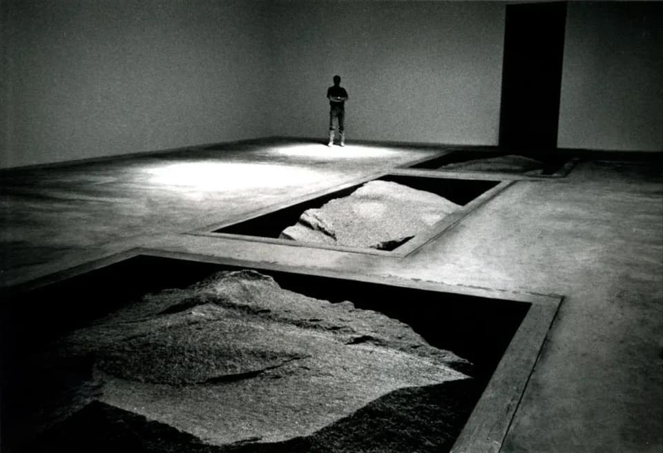 Minimalist gallery installation with concrete floor, geometric cutouts revealing sand layers below, stark lighting, and solitary figure, by Cross Architecture.