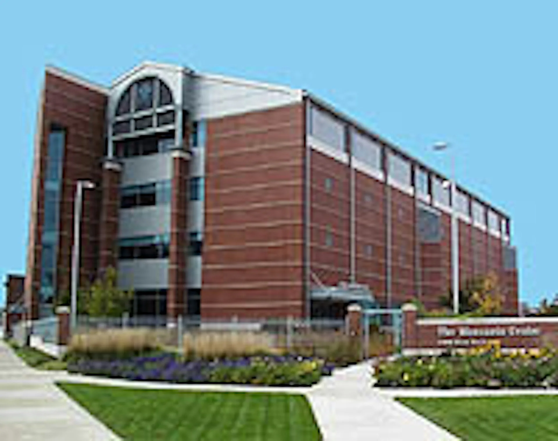 Modern brick institutional building with curved glass tower element, extensive glazing, and manicured landscaping designed by Croxton Collaborative.