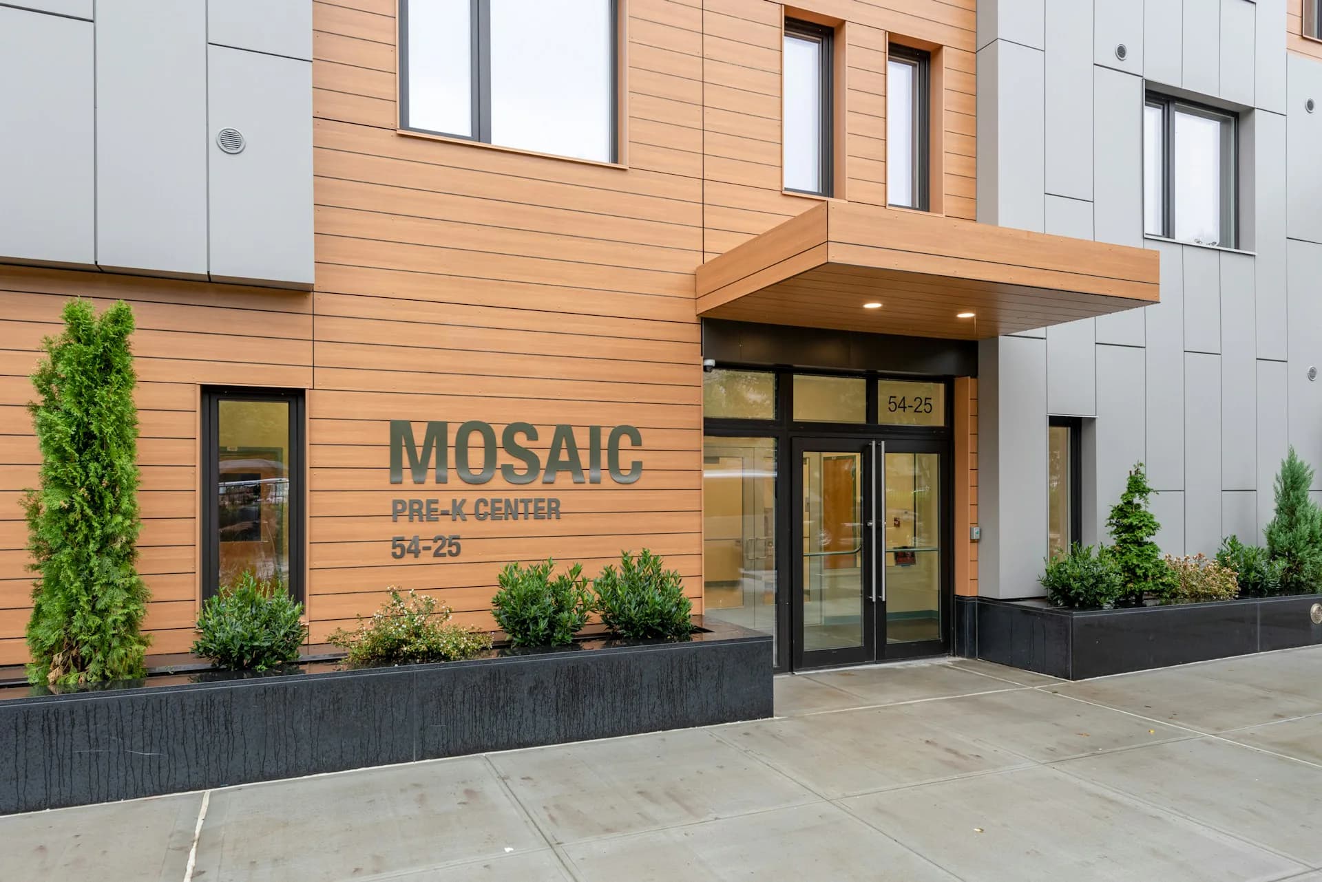 Modern residential building exterior with warm wood cladding, featuring the Mosaic apartment entrance, clean lines, and integrated landscaping by CTA Architects P.C.