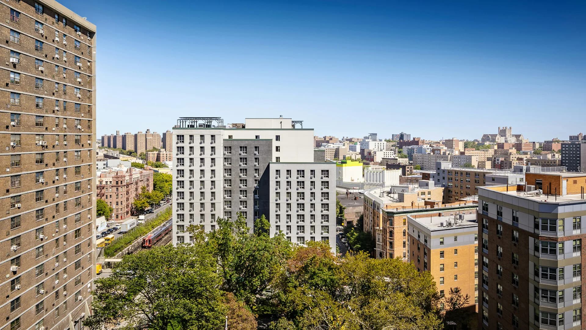 Urban residential buildings with brick and modern facades overlooking a dense Manhattan neighborhood under clear blue sky, by Curtis + Ginsberg Architects.