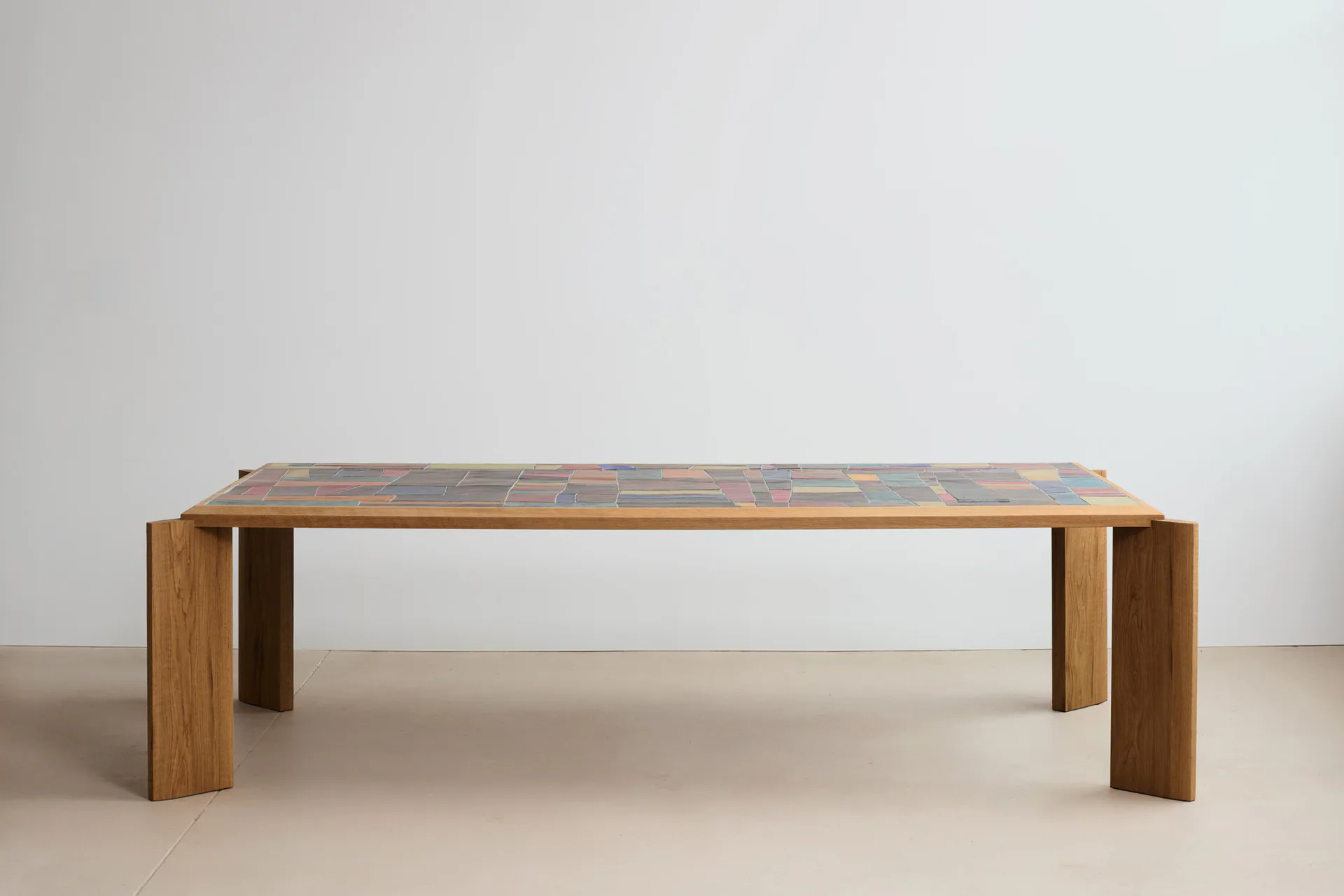 Minimalist wooden dining table with geometric tile inlay top and chunky rectangular legs on neutral background by D-Haene Studio.
