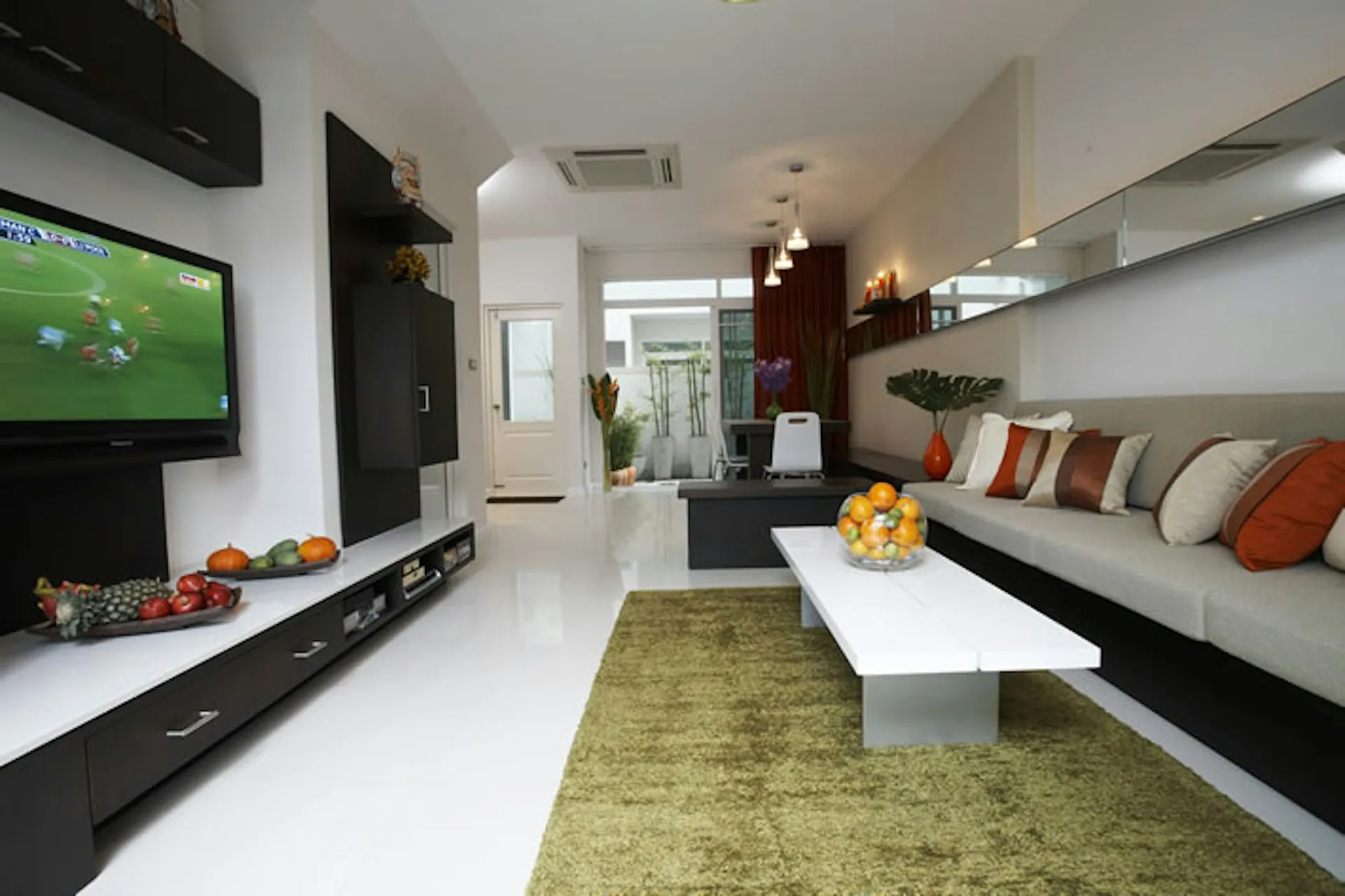 Modern living room with sleek black media console, white coffee table, olive green area rug, and built-in seating with colorful pillows by Daedalus Workshop LLC.