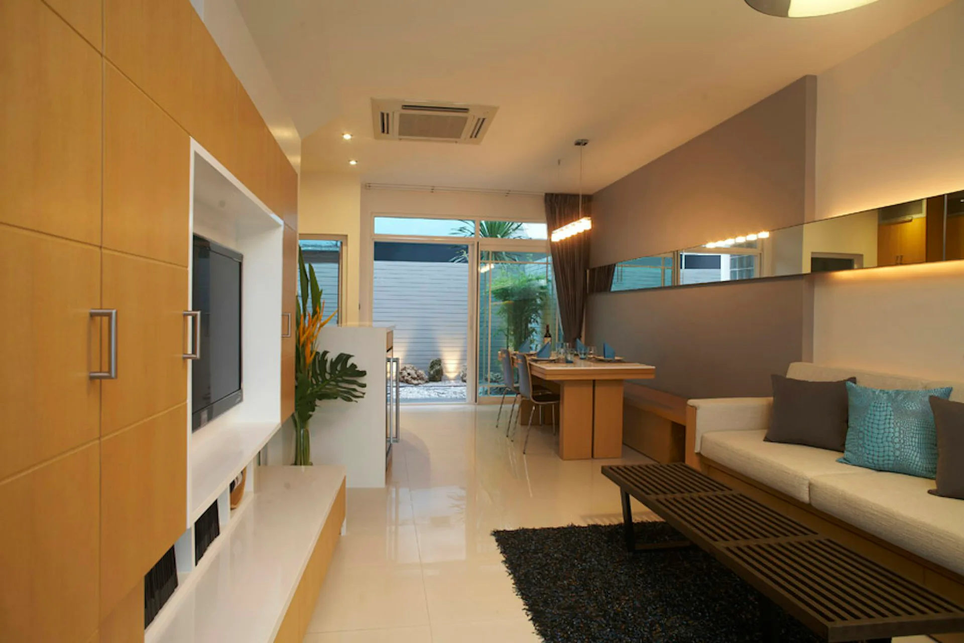 Modern residential interior featuring warm wood cabinetry, cream flooring, built-in seating with turquoise accents, and natural lighting from floor-to-ceiling windows by Daedalus Workshop LLC.
