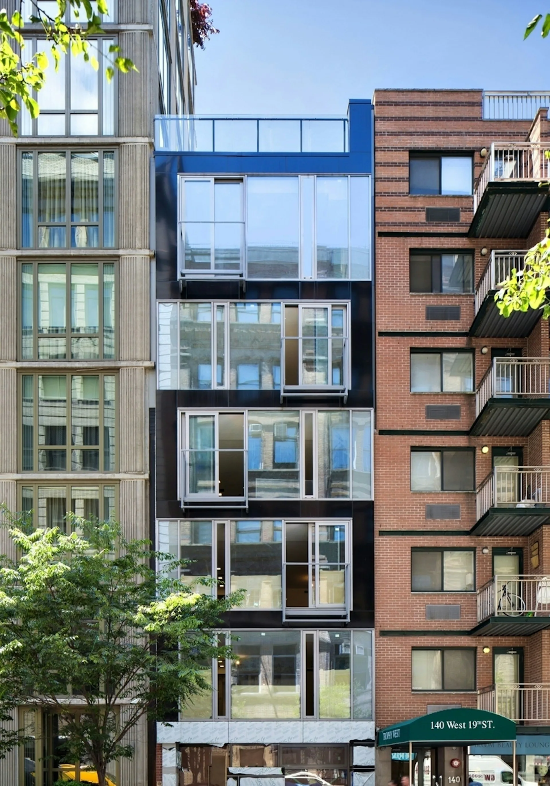 Narrow infill residential building with dark metal and glass facade nestled between classical stone and modern brick buildings on a New York street by Daniel Goldner Architects.