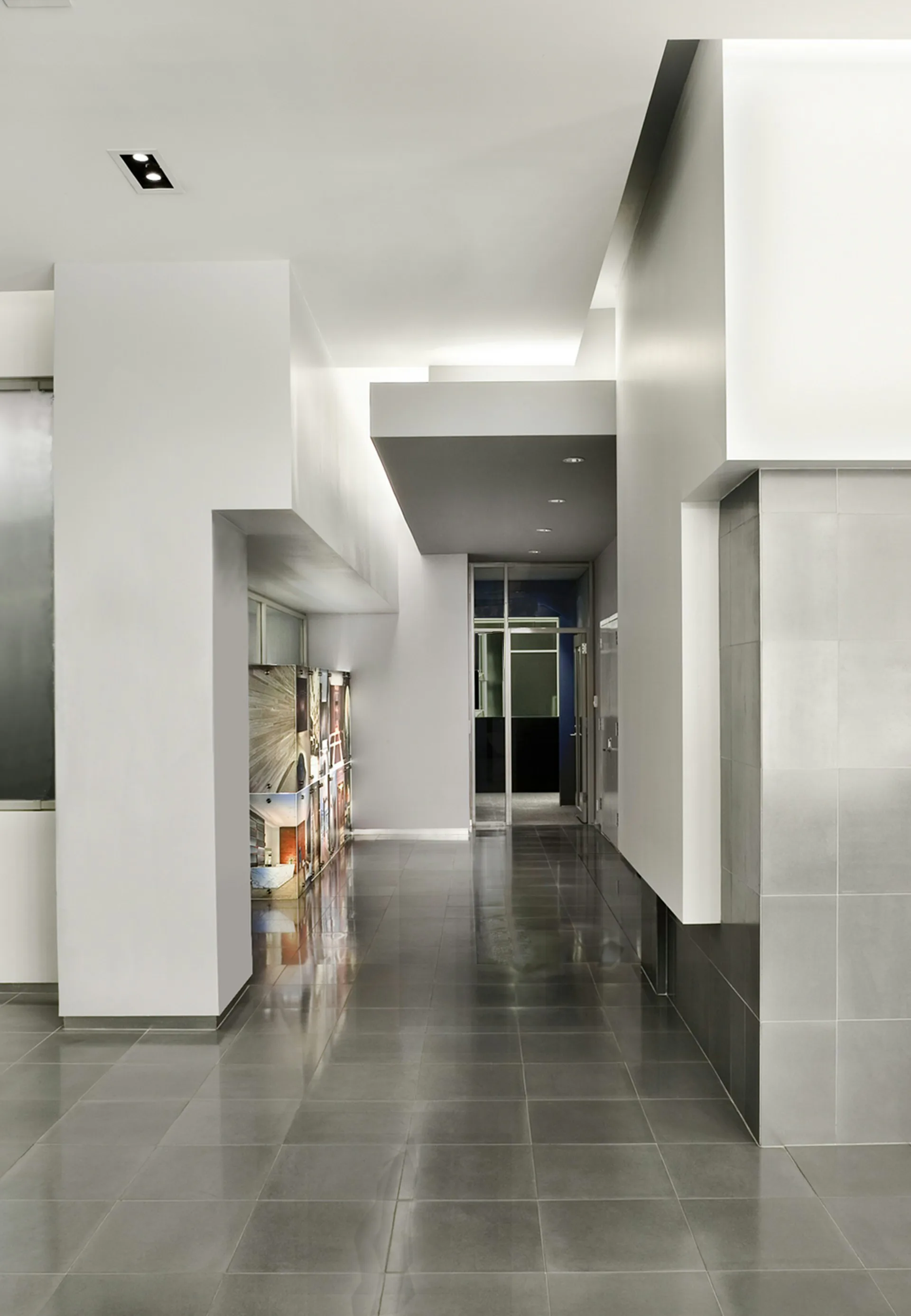 Minimalist corridor with polished dark flooring, white walls, and geometric ceiling elements with skylights by Daniel Goldner Architects.