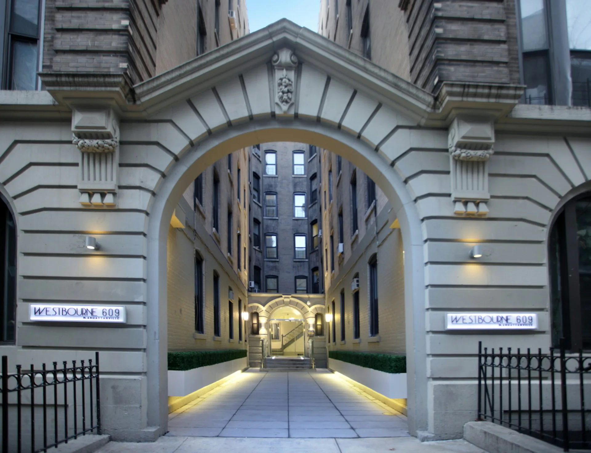 Illuminated archway passage with classical stone facade, symmetrical design, and warm lighting leading through to a modern urban courtyard by Daniel Goldner Architects.