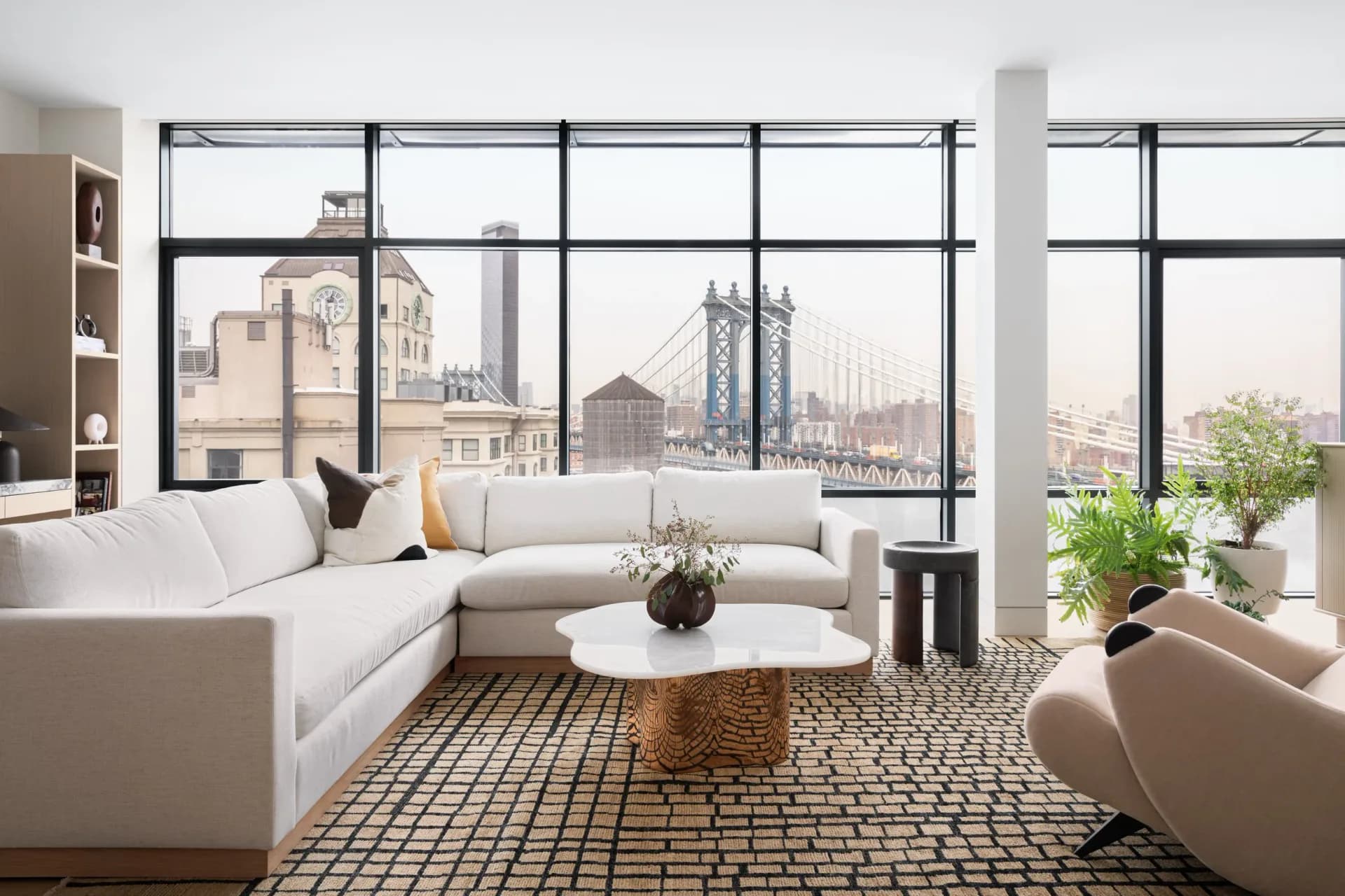 Modern high-rise living room with floor-to-ceiling windows overlooking a city skyline, featuring a white sectional sofa, geometric patterned rug, and contemporary furnishings by Danielle Colding Design.