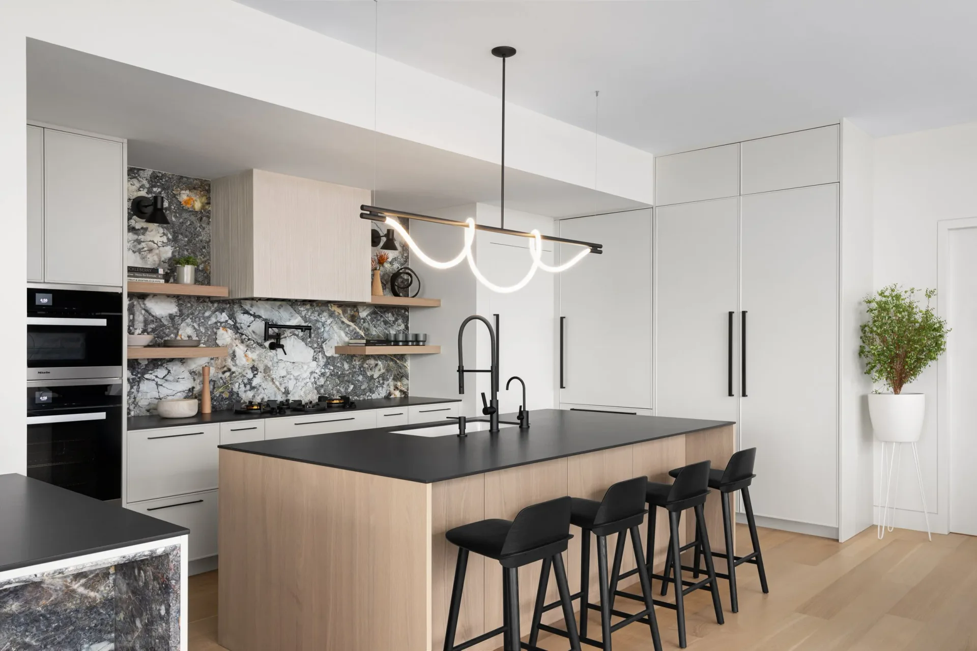 Modern white kitchen with wood and black island, marble backsplash, black appliances, and pendant lighting by Danielle Colding Design.