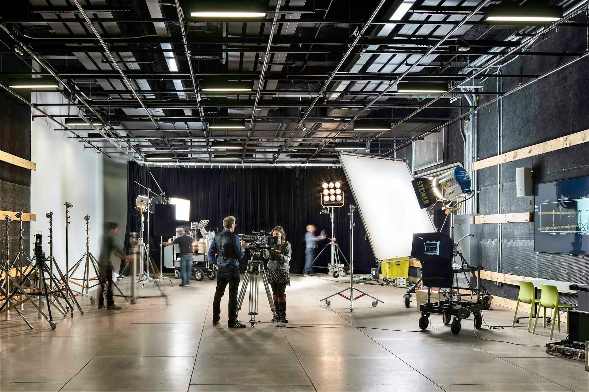 Professional television and film production studio with industrial ceiling, professional lighting rigs, and crew members setting up equipment, designed by Dattner Architects.