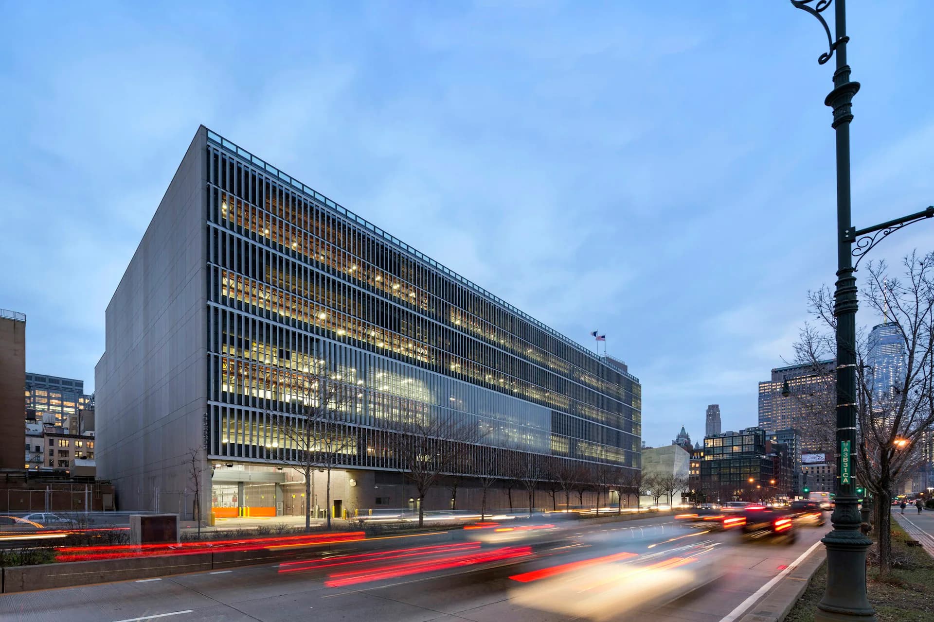 Modern multi-story office building with dark facade and illuminated interior at dusk, surrounded by urban streetscape and traffic, designed by Dattner Architects.