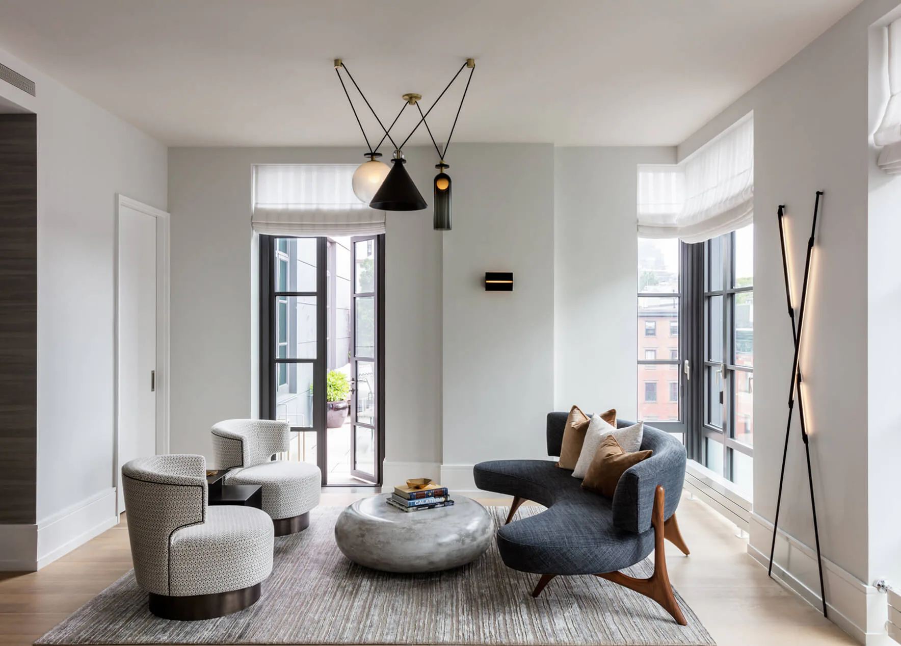 Bright modern living room with gray and cream seating, concrete side table, geometric pendant lighting, and wood floors by DHD Architecture & Interior Design.