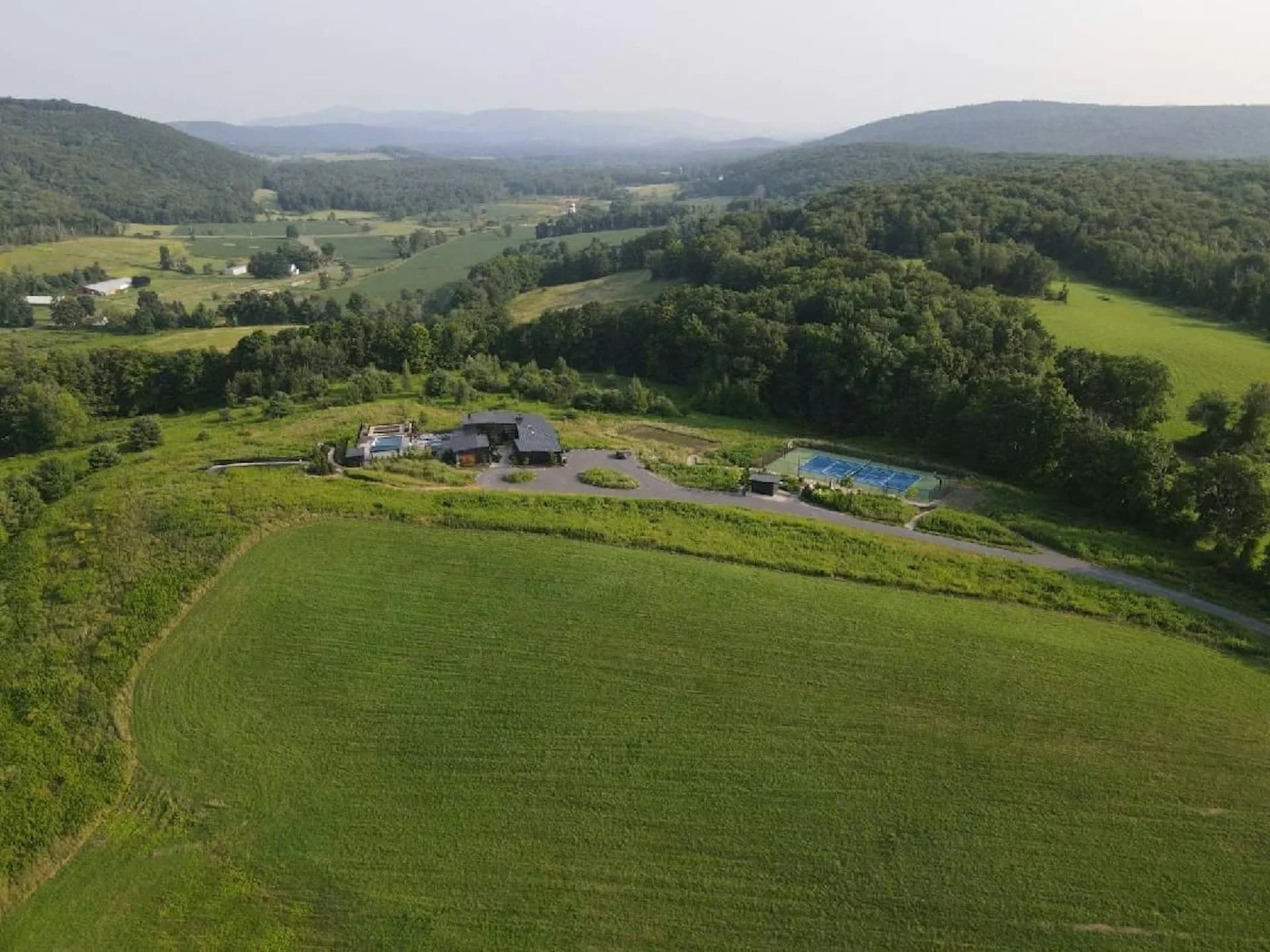 Aerial view of a contemporary residential compound nestled in a verdant valley with manicured lawns, surrounded by forested hills and distant mountains, by David Jay Weiner, Architects.