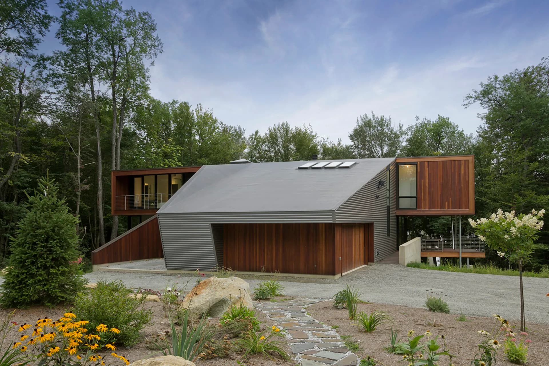 Modern residential architecture featuring corrugated metal siding and wood accents nestled among trees, with a sloped roof and landscaped grounds by David Jay Weiner, Architects.