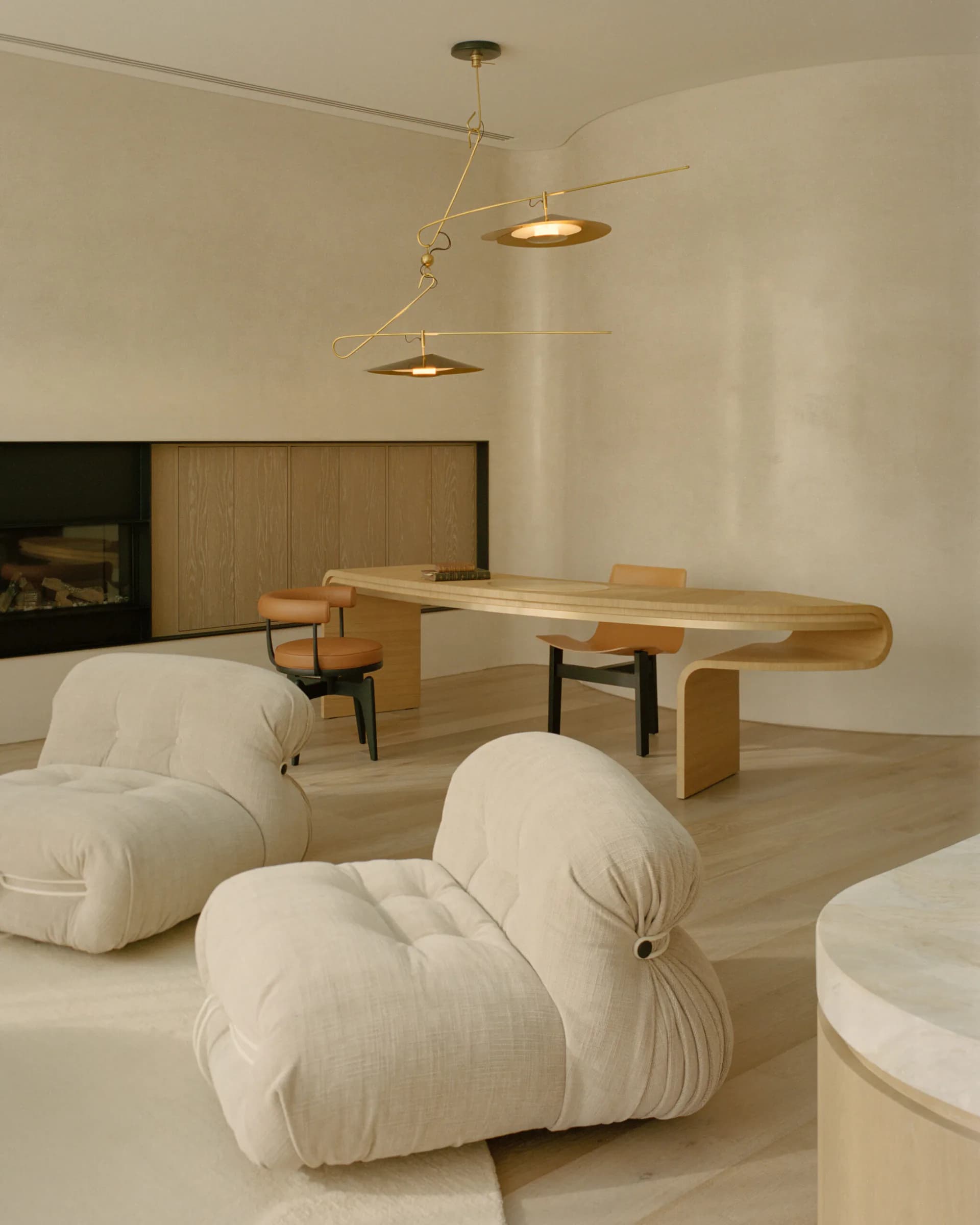 Minimalist interior space with cream puffy sculptural seating, wooden table, and brass pendant lighting by David Weeks Studio.