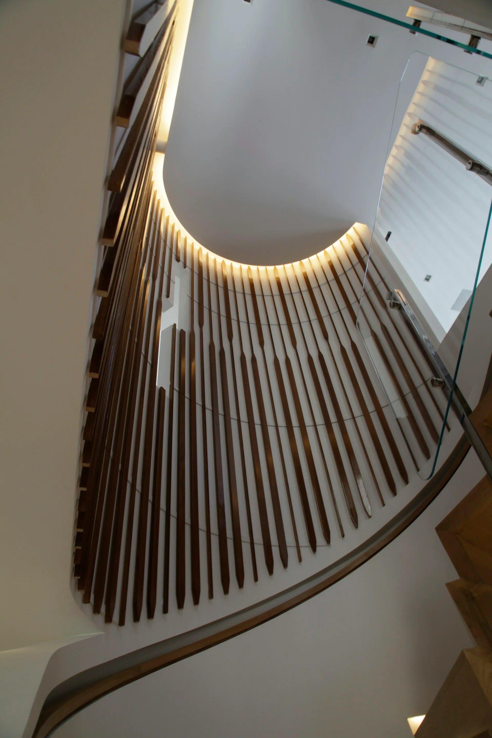 Curved stairwell with wooden slat railings and integrated warm lighting design by David Yum Architects.