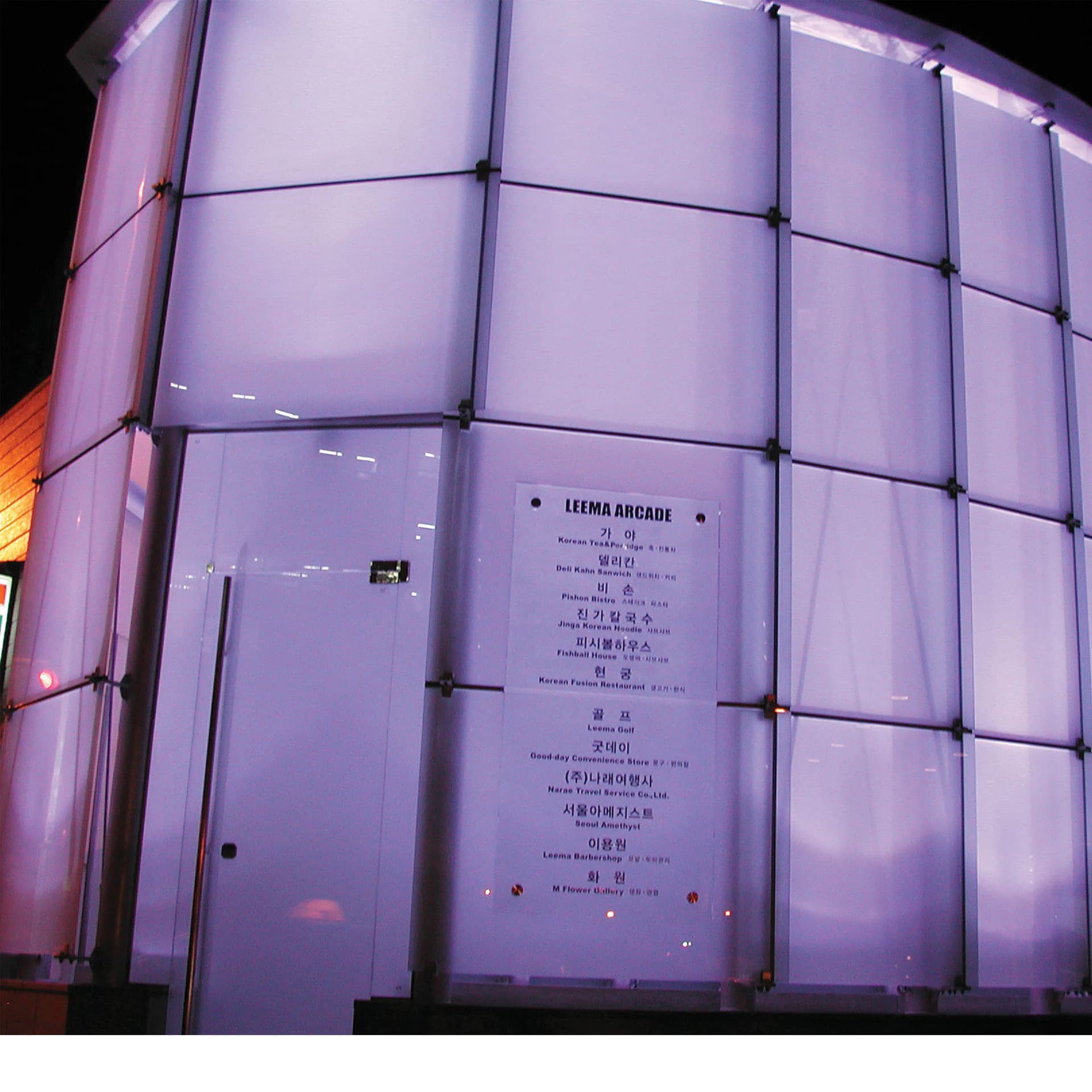 Illuminated facade of Luma Arcade with translucent purple-tinted panels and integrated signage by David Yum Architects.