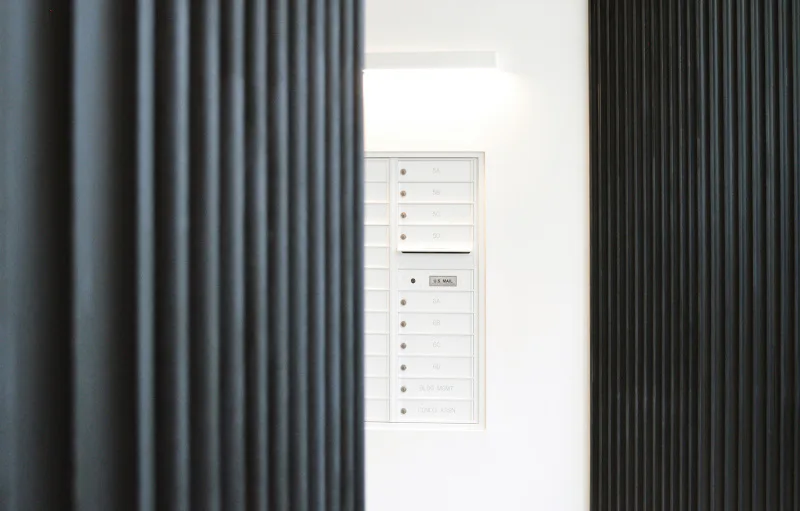 Minimalist interior with vertical pleated curtains in charcoal and light gray flanking a white wall-mounted electrical panel by Davies Toews.