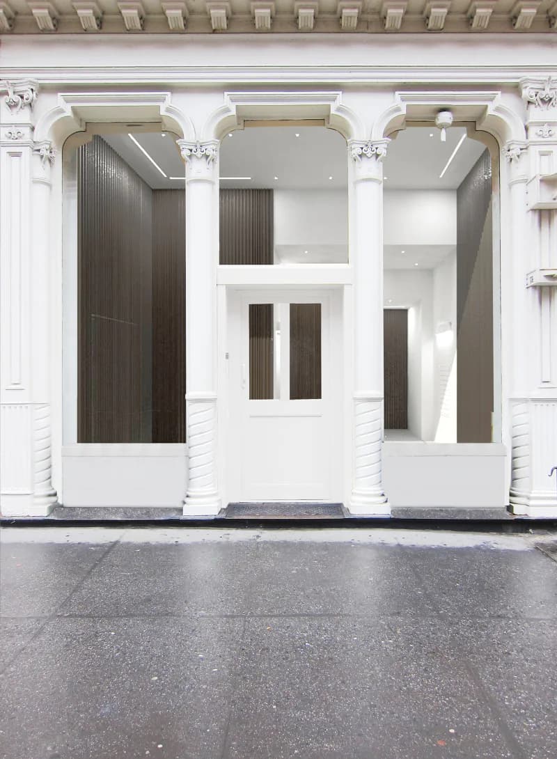 Minimalist storefront facade with three bays featuring white columns, dark wood doors and panels, and ornamental cornicing, designed by Davies Toews.