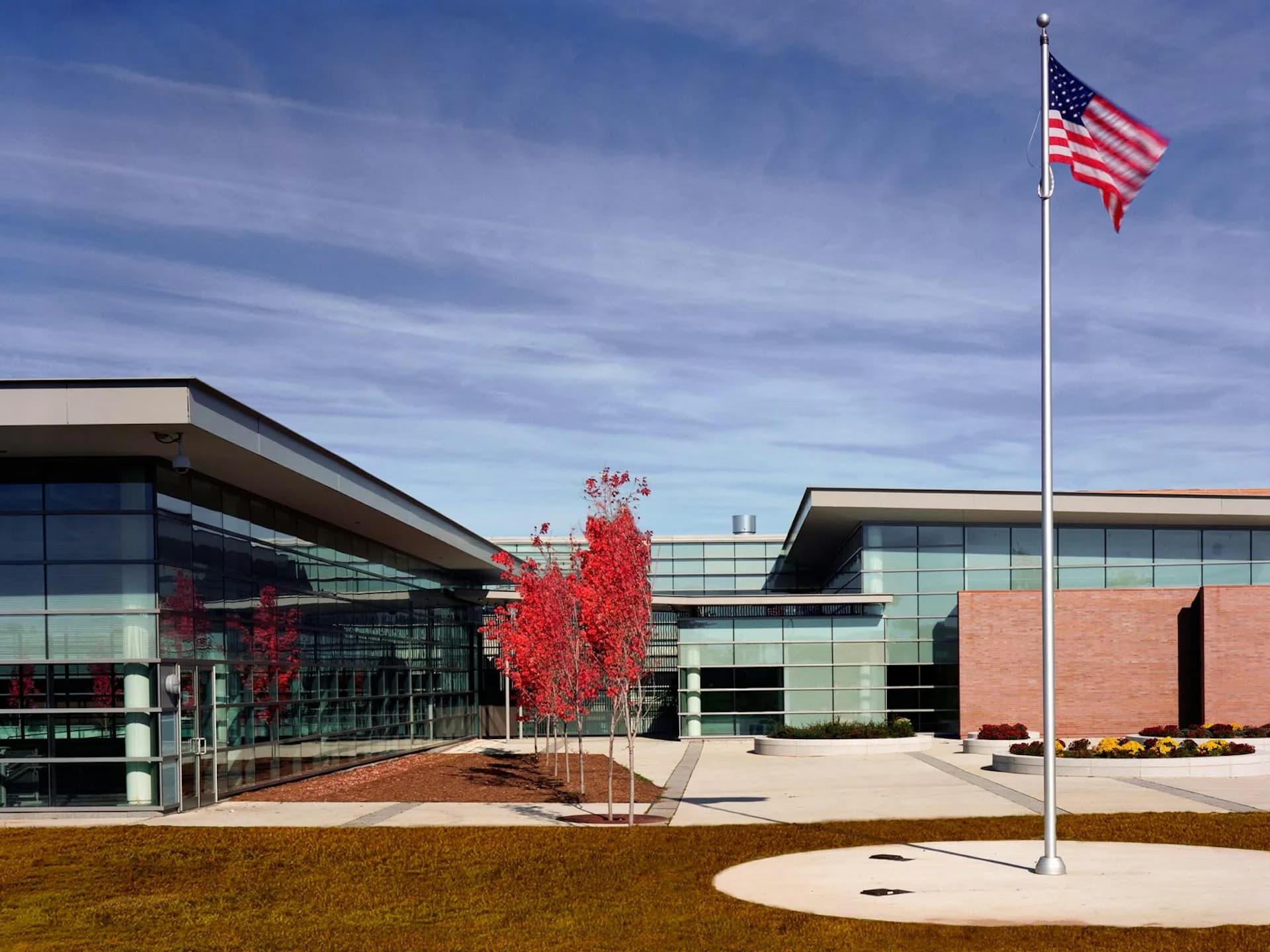 Modern institutional building with glass and brick facades, red ornamental tree, and flagpole in courtyard landscape by Davis Brody Bond, a Page Company.