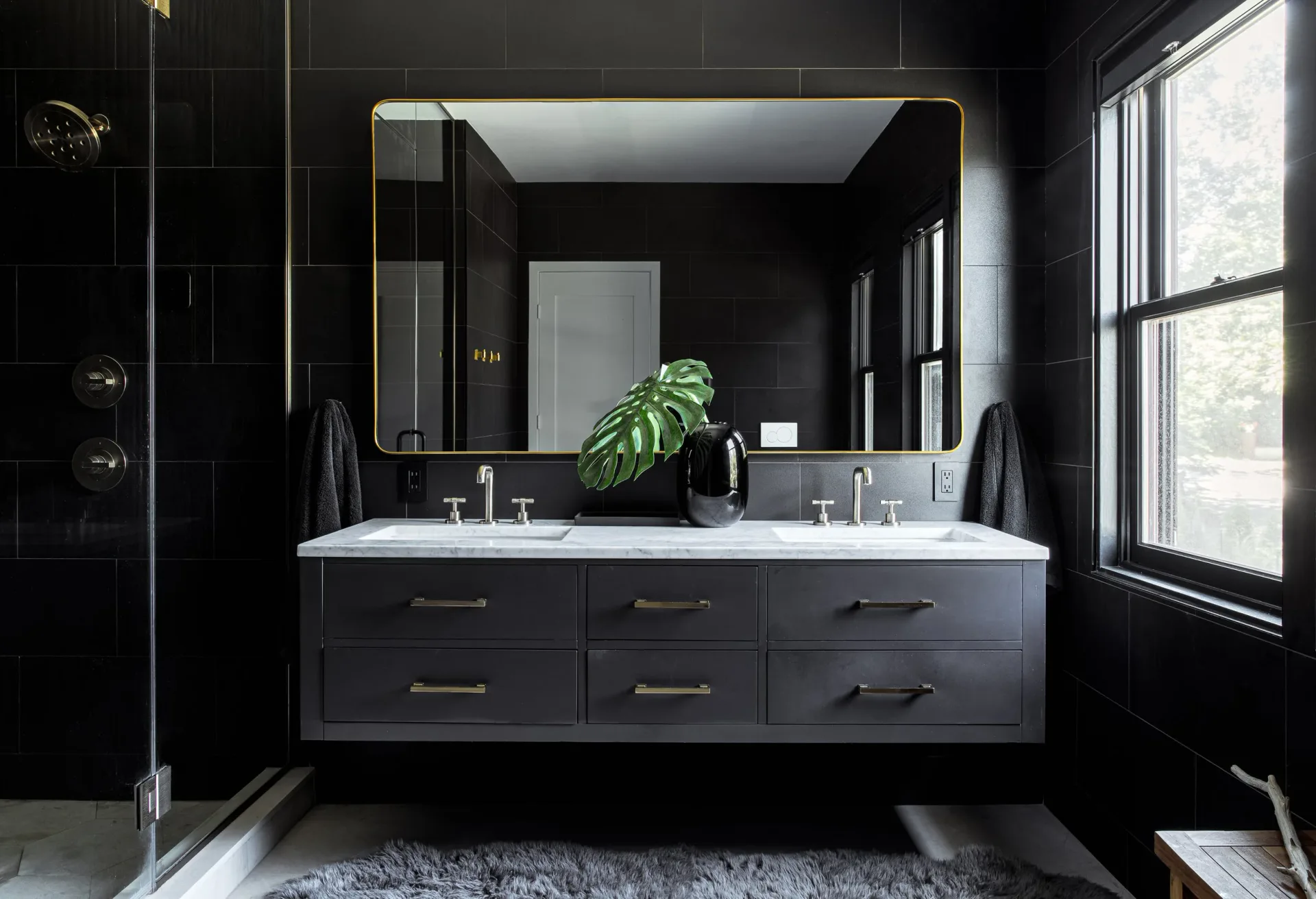 Luxe black bathroom vanity with dual sinks, large illuminated mirror, and natural light from windows, designed by Delia Kenza Interiors.
