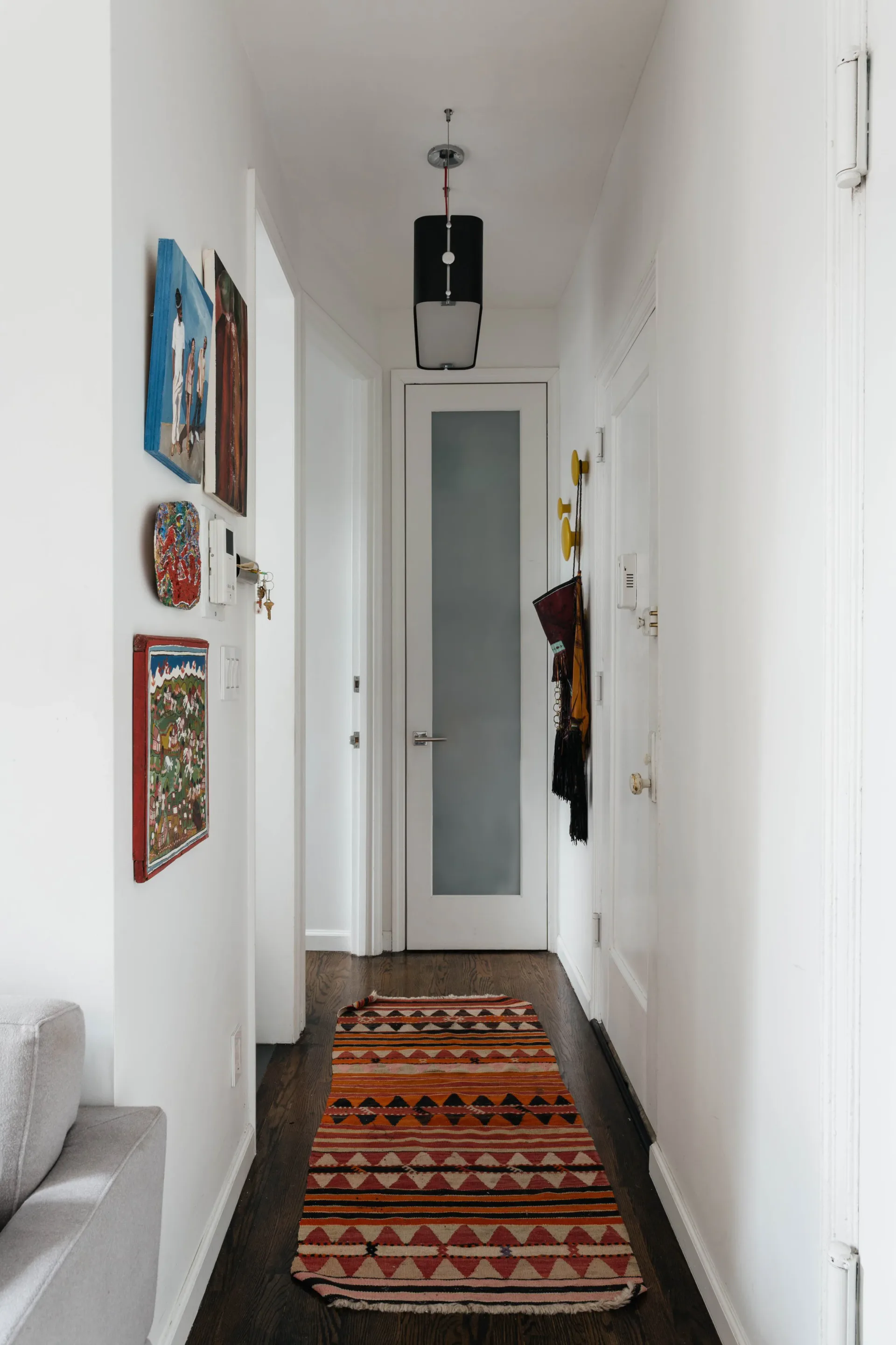 Narrow hallway with dark wood flooring, white walls, geometric patterned runner rug, pendant lighting, and curated wall art by Delia Kenza Interiors.